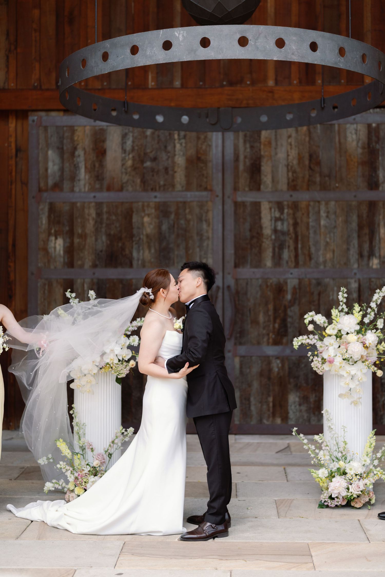 Romantic wedding couple poses in rustic barn setting with floral arch decorations.
