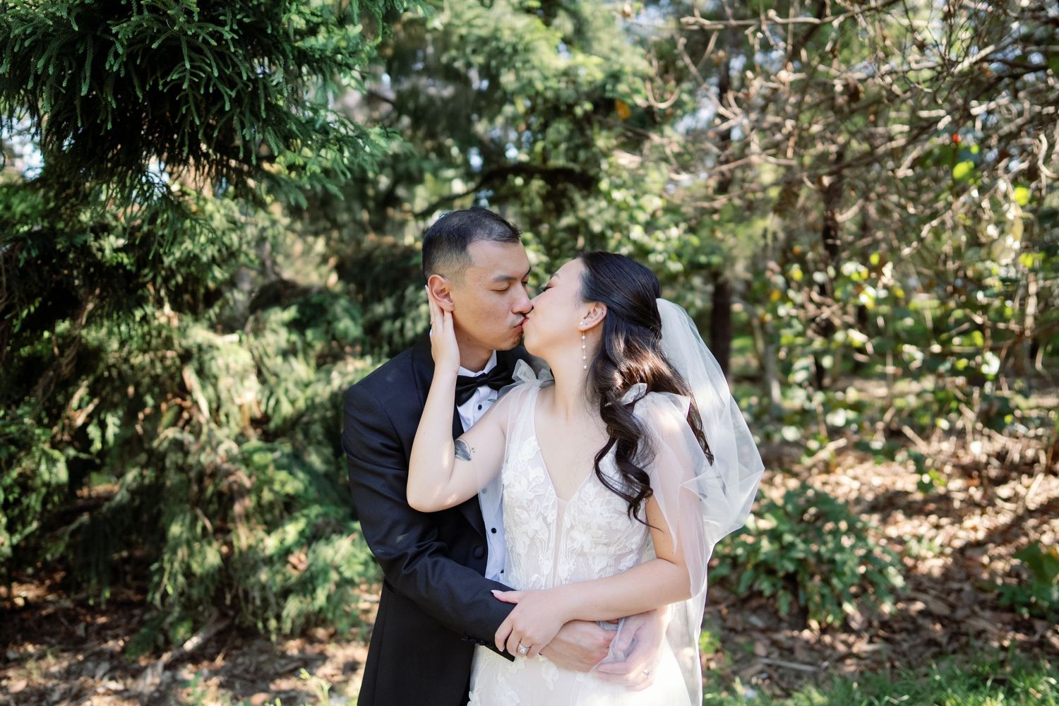 A bride and groom share an intimate moment in a garden setting with lush greenery.
