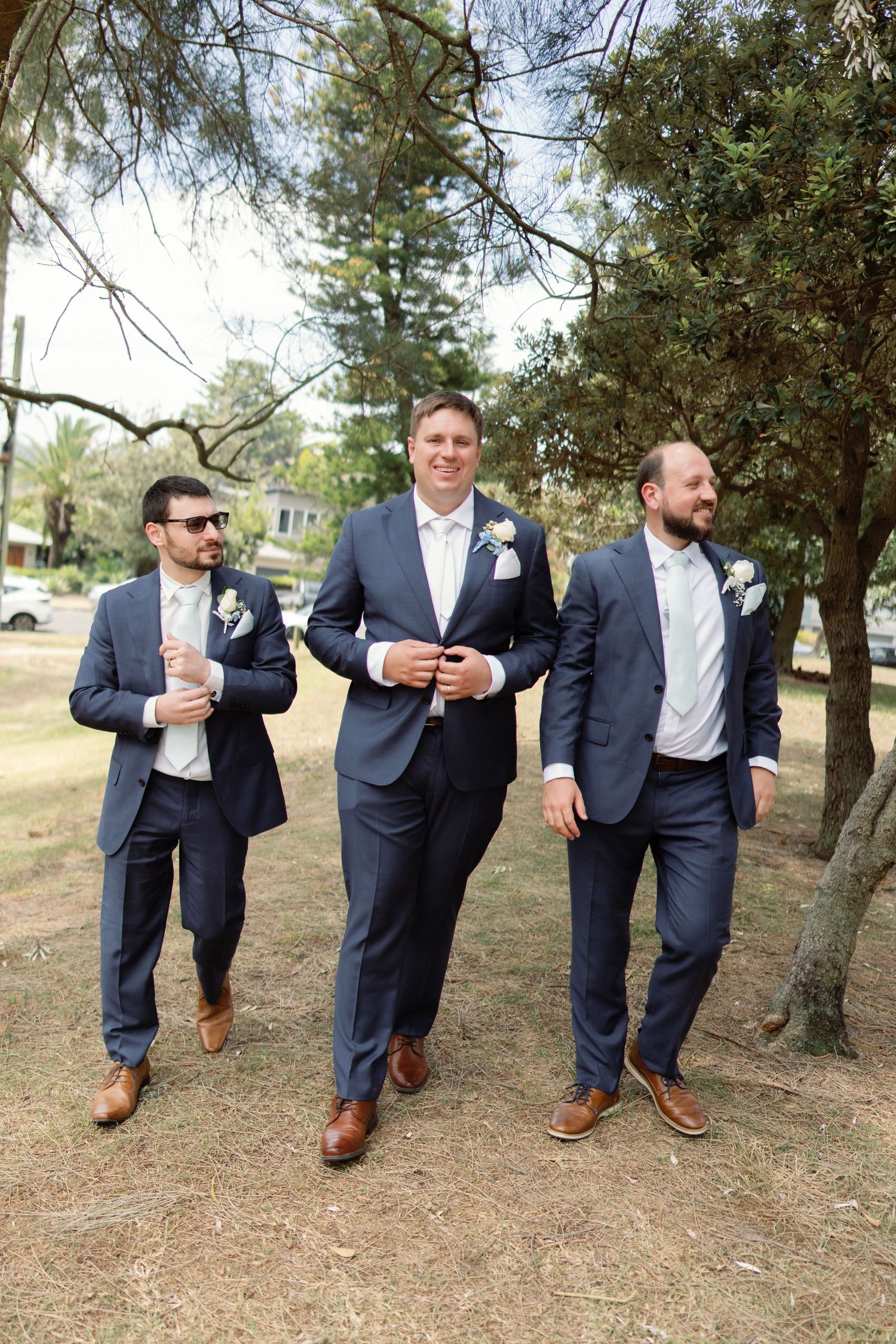 Wedding party in navy suits walking together on a grassy hill.