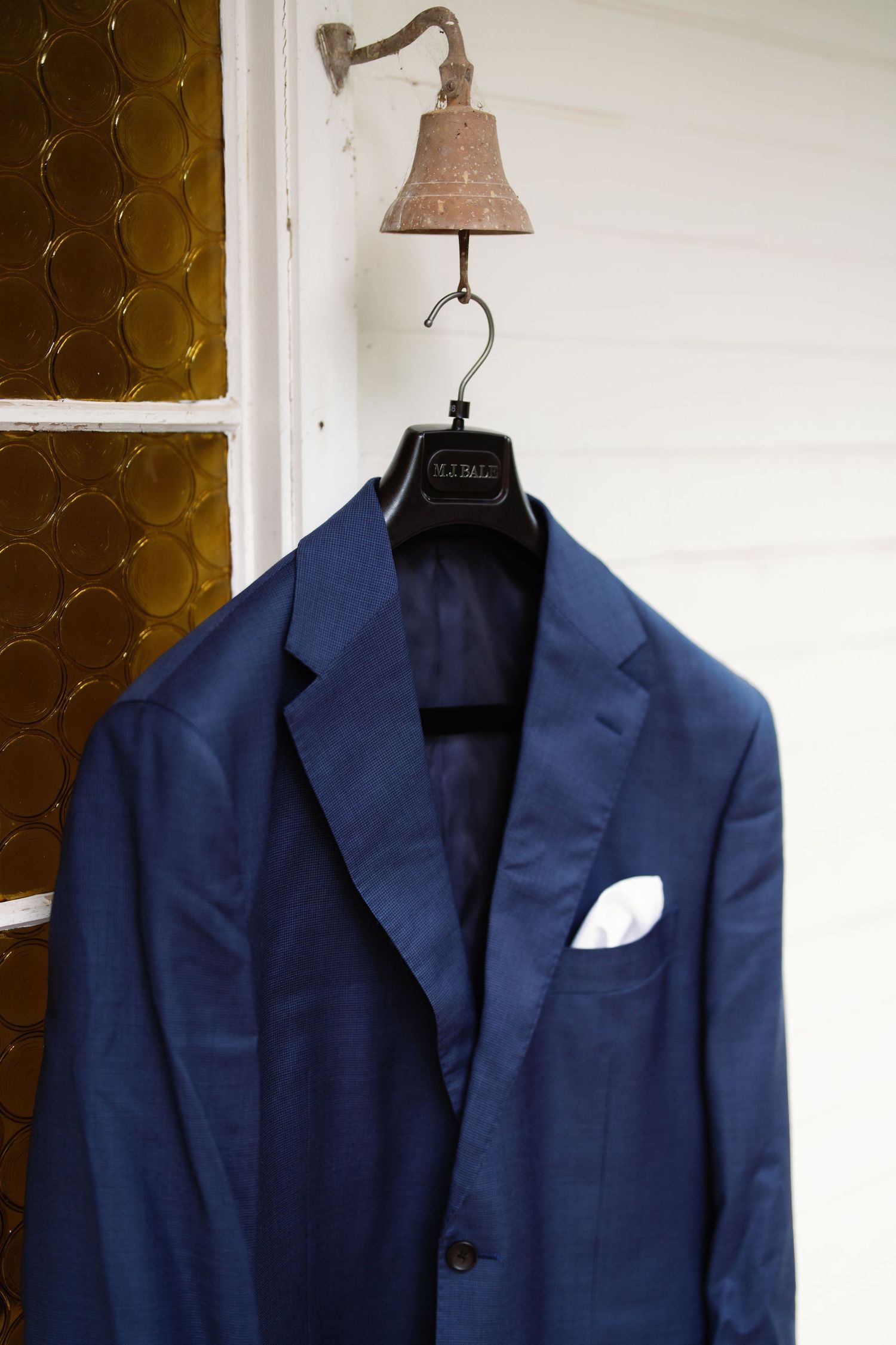 Navy blue suit jacket with white pocket square displayed on a hanger against a white wall.