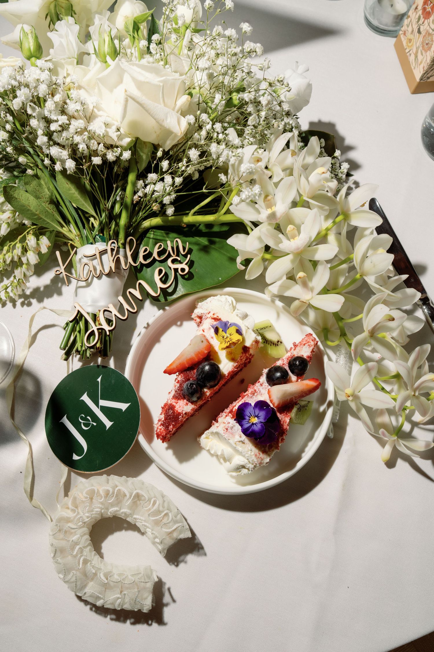 Wedding reception table with white floral arrangement, cake slices topped with berries, and J&K monogram decor.