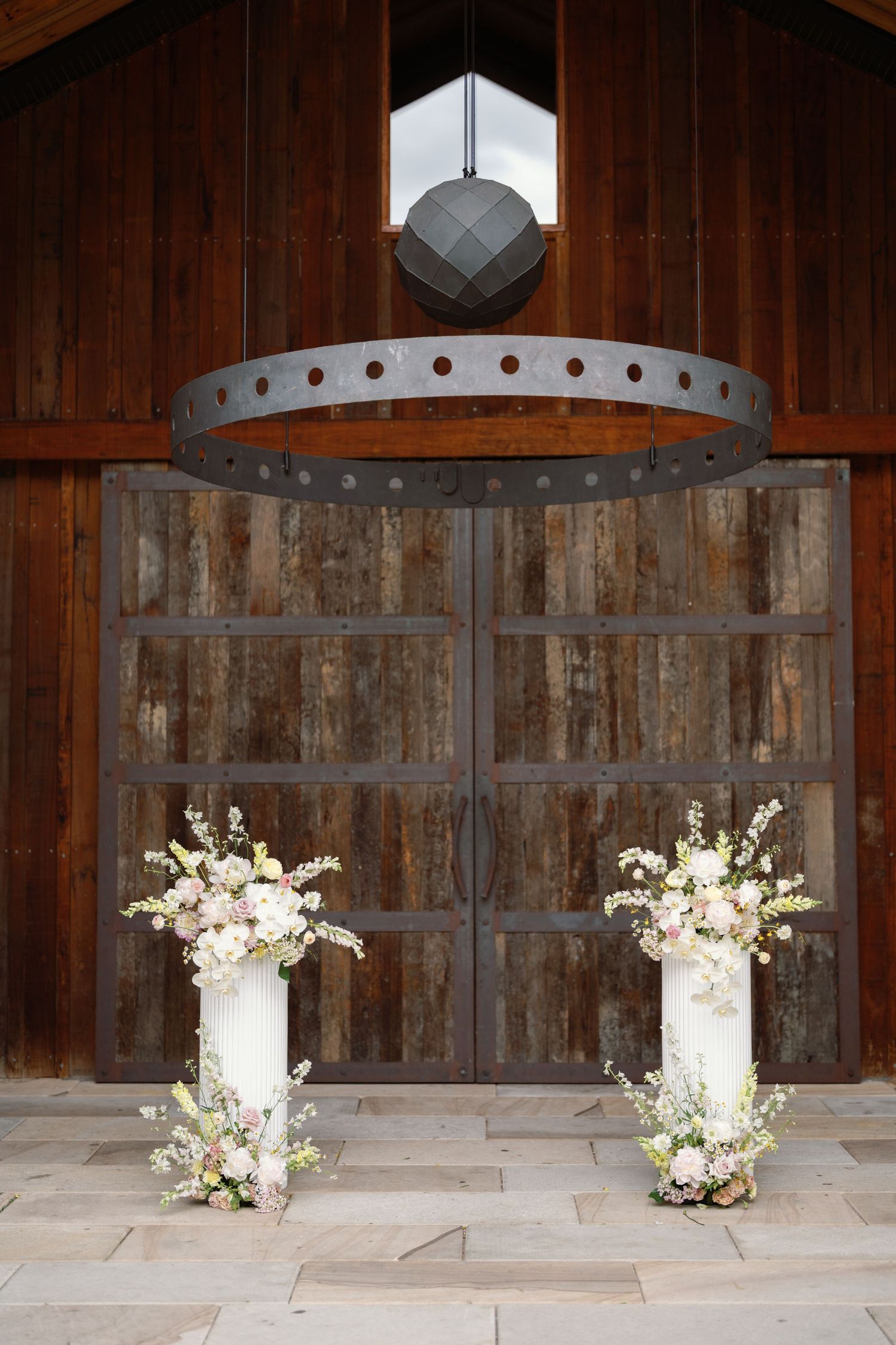 Elegant white floral arrangements in tall vases decorate a rustic wooden barn interior setting.