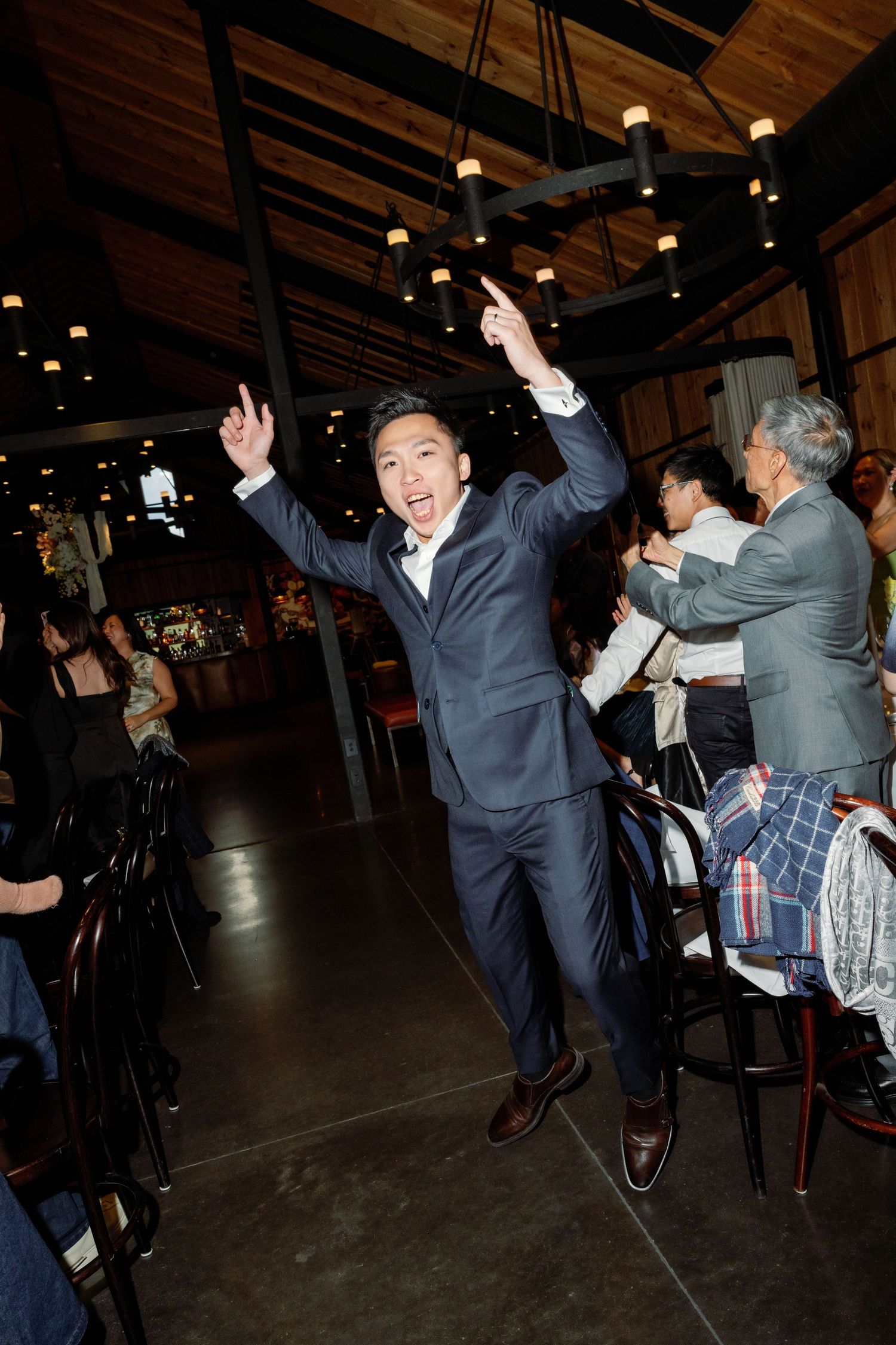 Wedding reception guests dancing and celebrating in a dimly lit rustic venue.