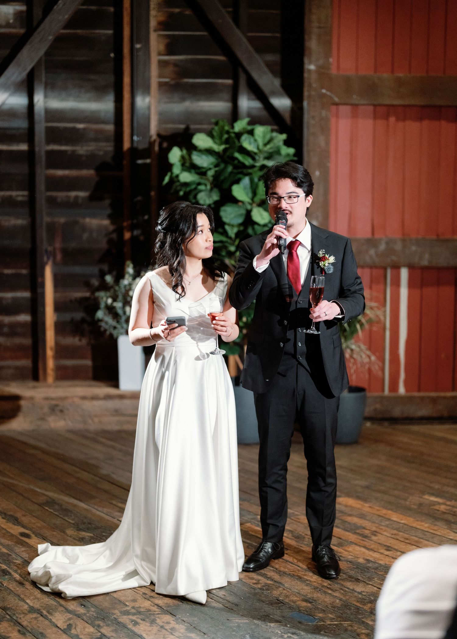 A couple shares a romantic moment on a rustic wooden deck with red barn walls in the background.