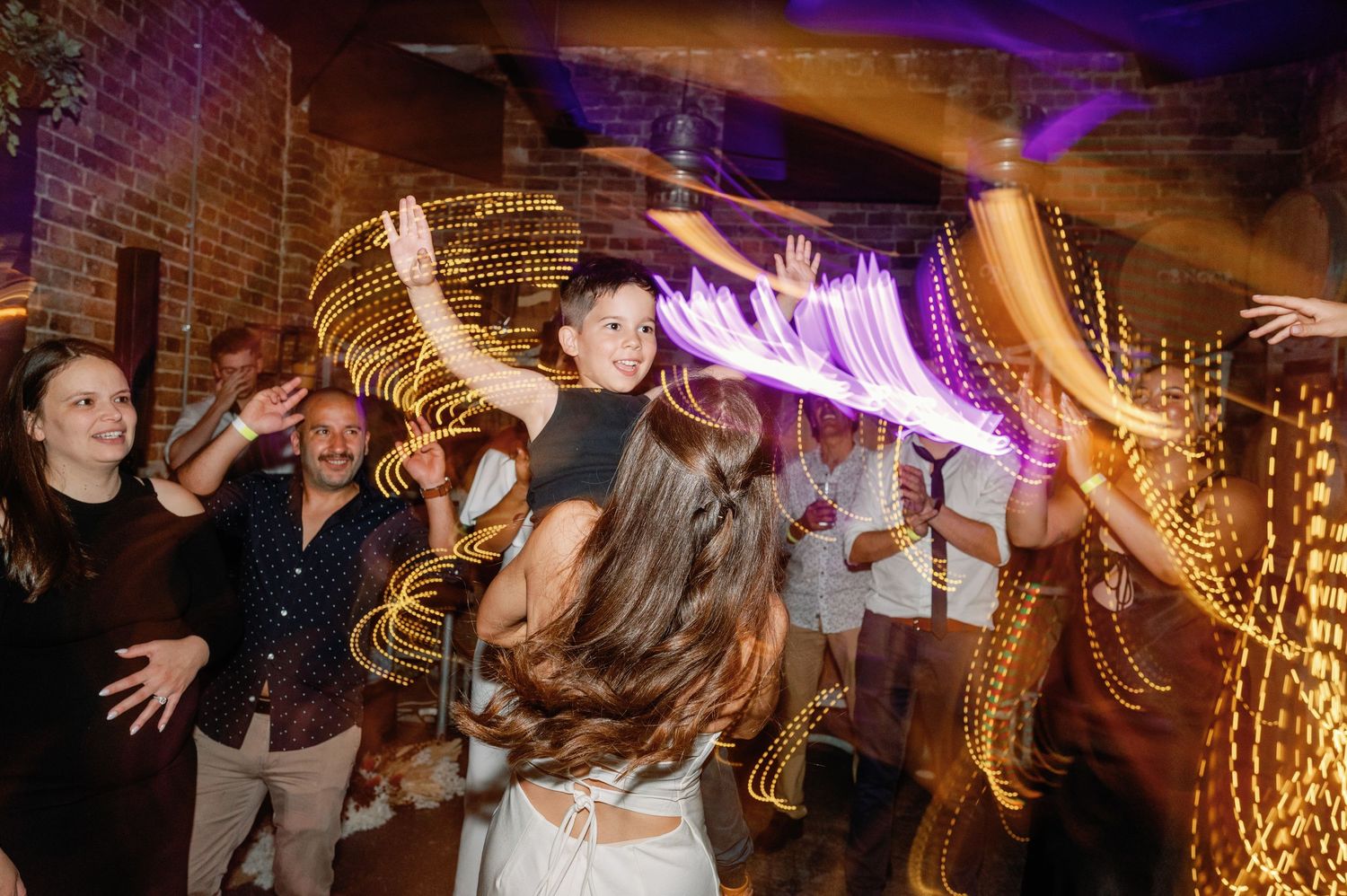 Partygoers dance beneath decorative lighting in an industrial-style event space.