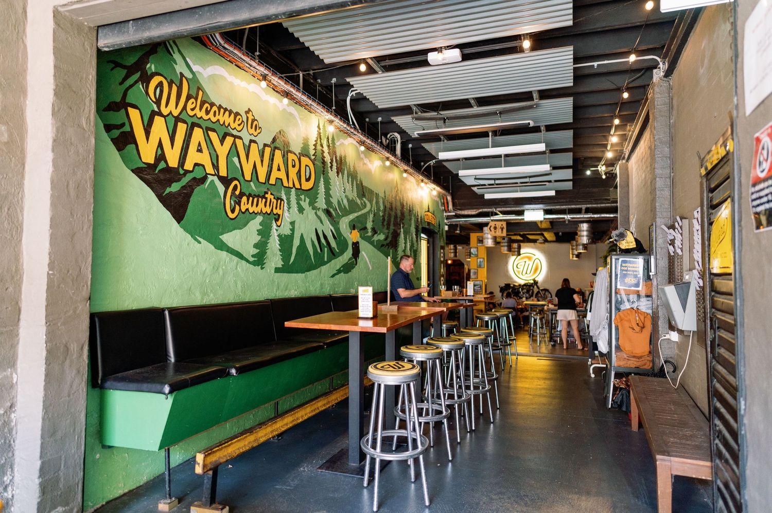Long corridor in a brewery or bar with wooden barrels and neon signage.