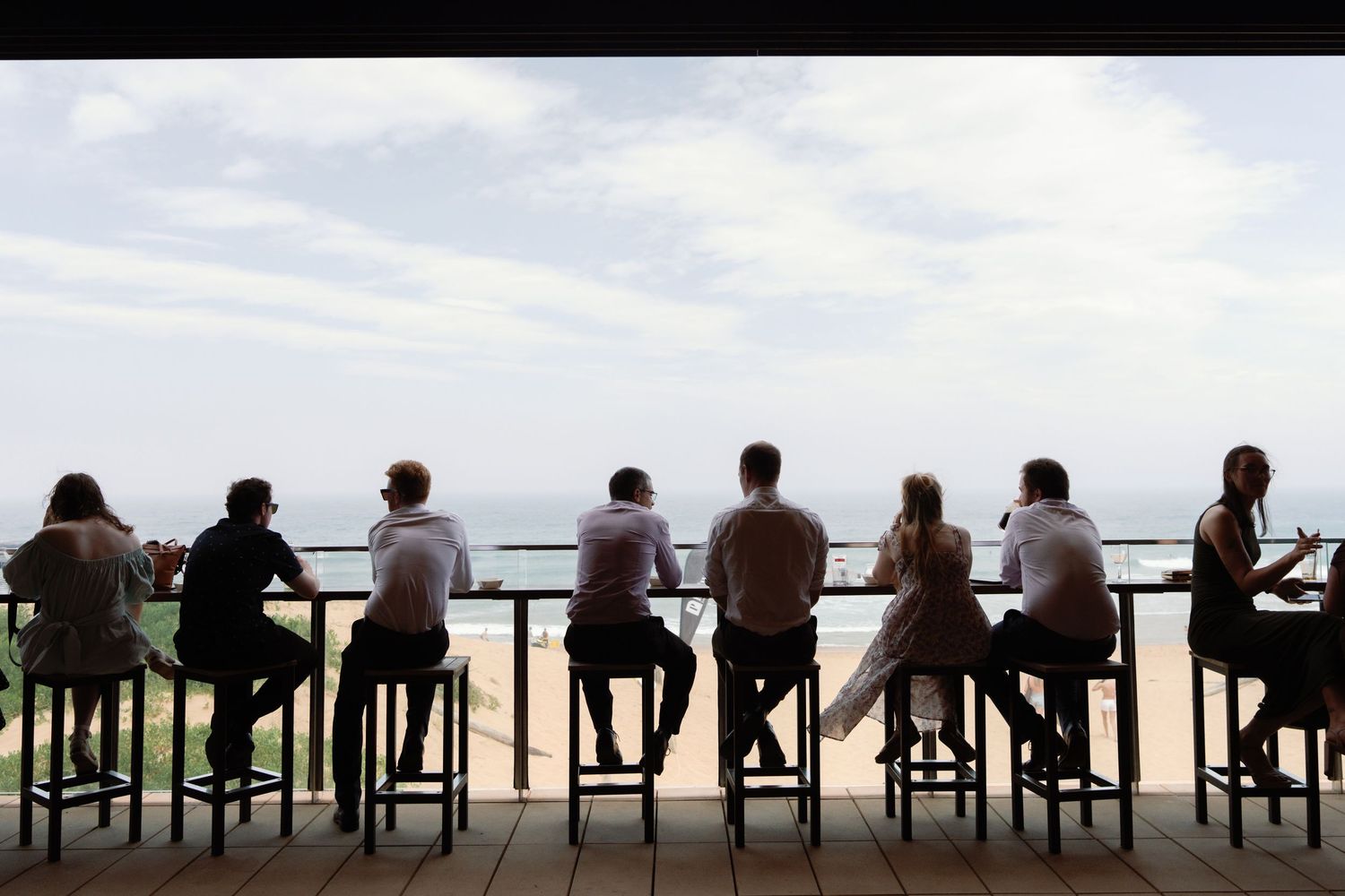 Silhouetted people sit in a row of chairs against a bright sky background.