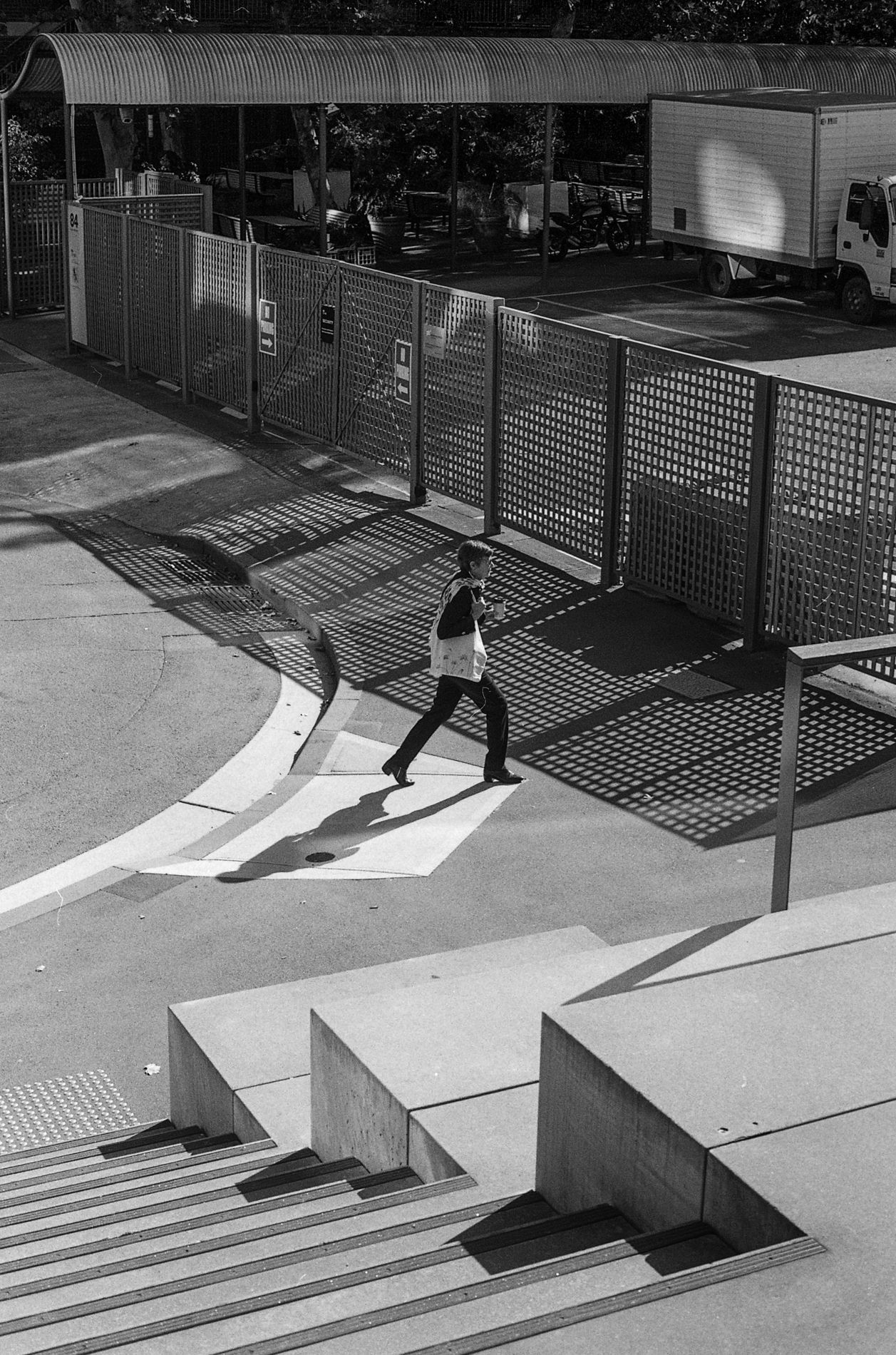 Person walking across a pedestrian crossing near metal barriers in black and white.