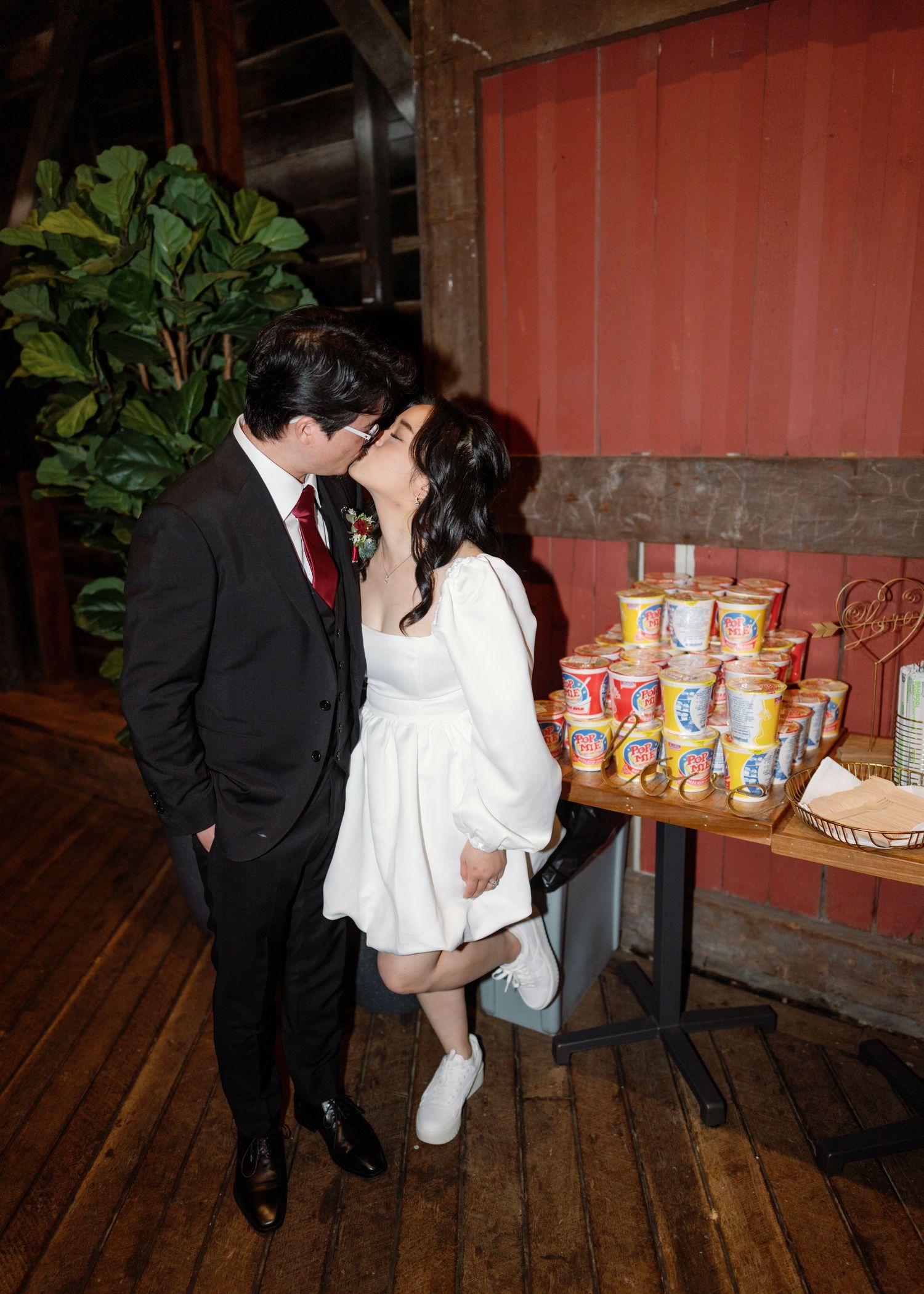 Wedding couple sharing tender moment in rustic wooden setting with snacks displayed.