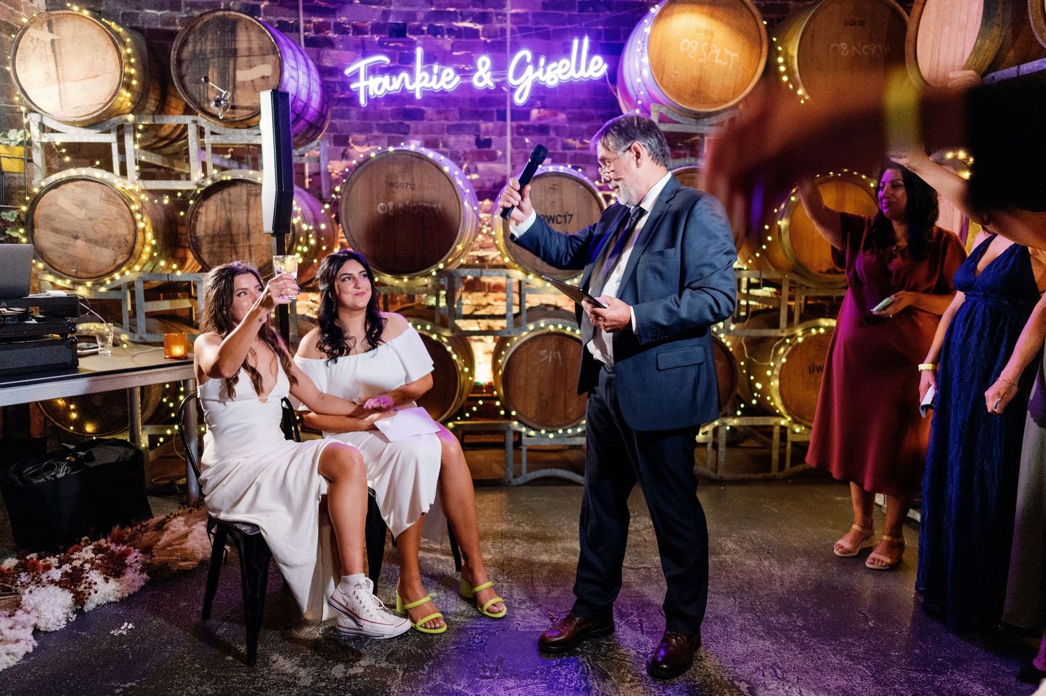 Wedding party dancing and celebrating in a rustic barrel room with purple ambient lighting.