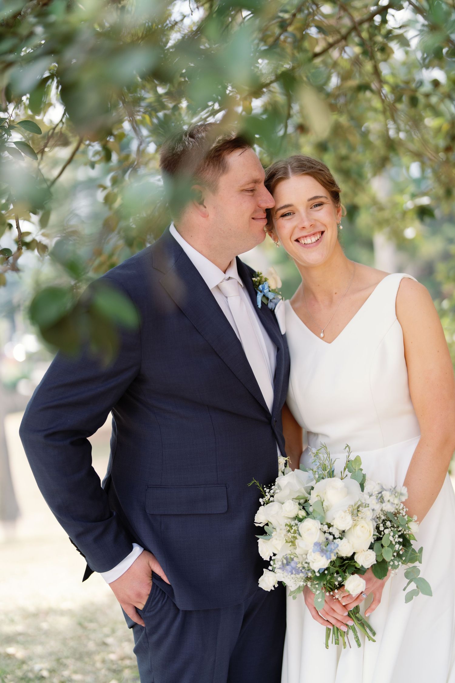 Romantic outdoor wedding portrait under green trees.