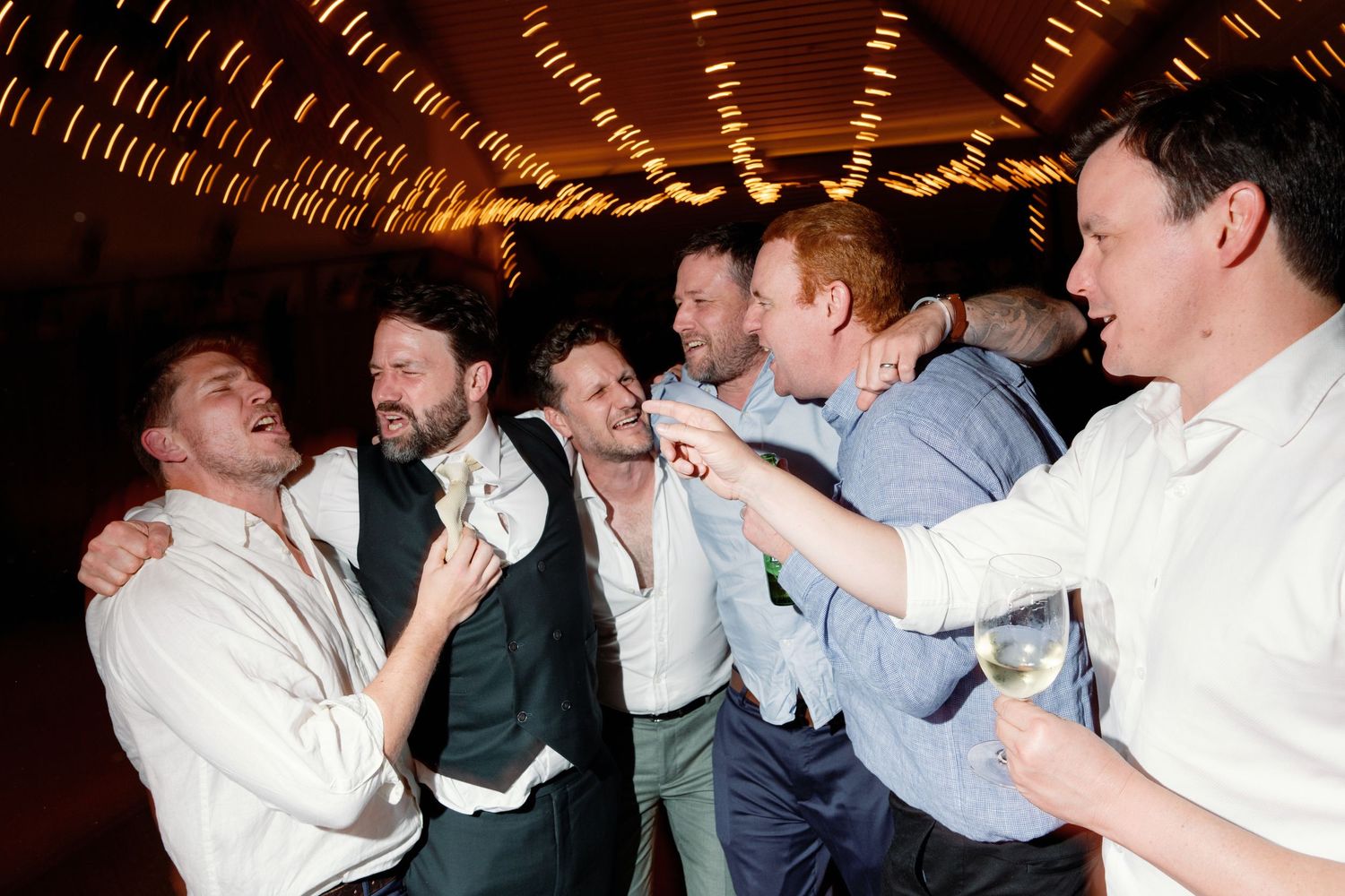 Group of men laughing and celebrating together at lively wedding reception party.