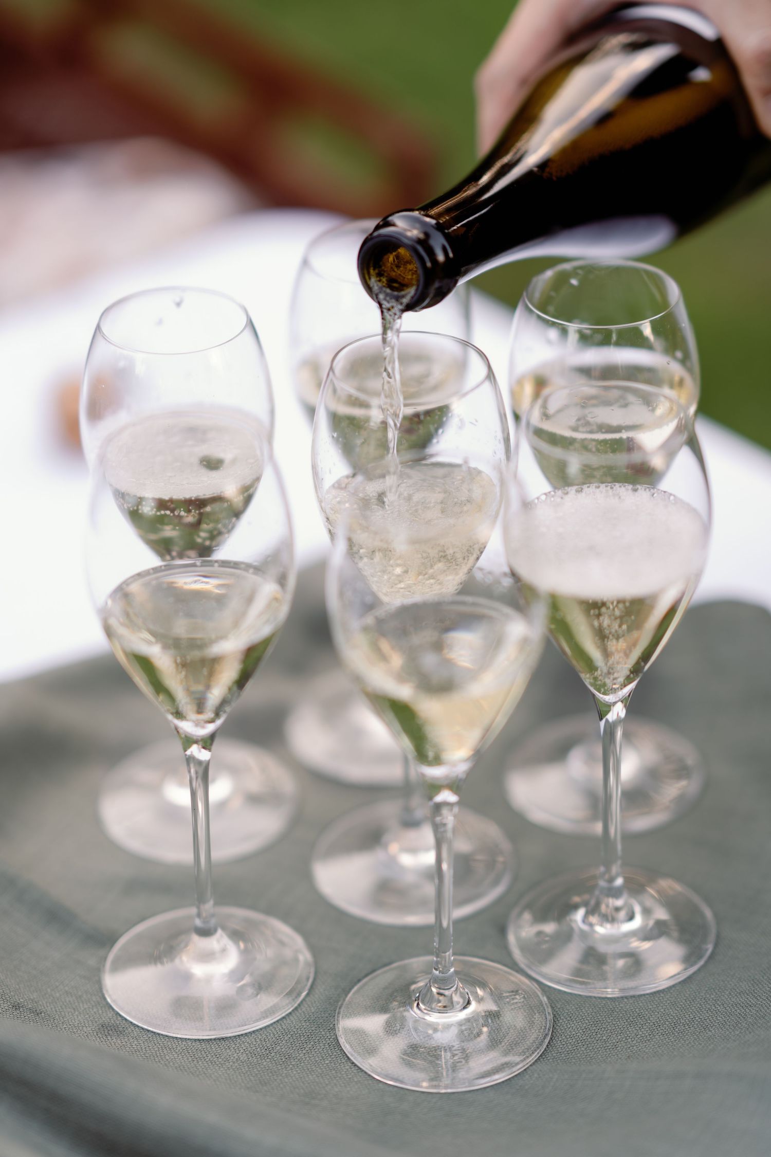 Champagne being poured from a dark bottle into elegant flute glasses arranged on a tray at a celebration event.