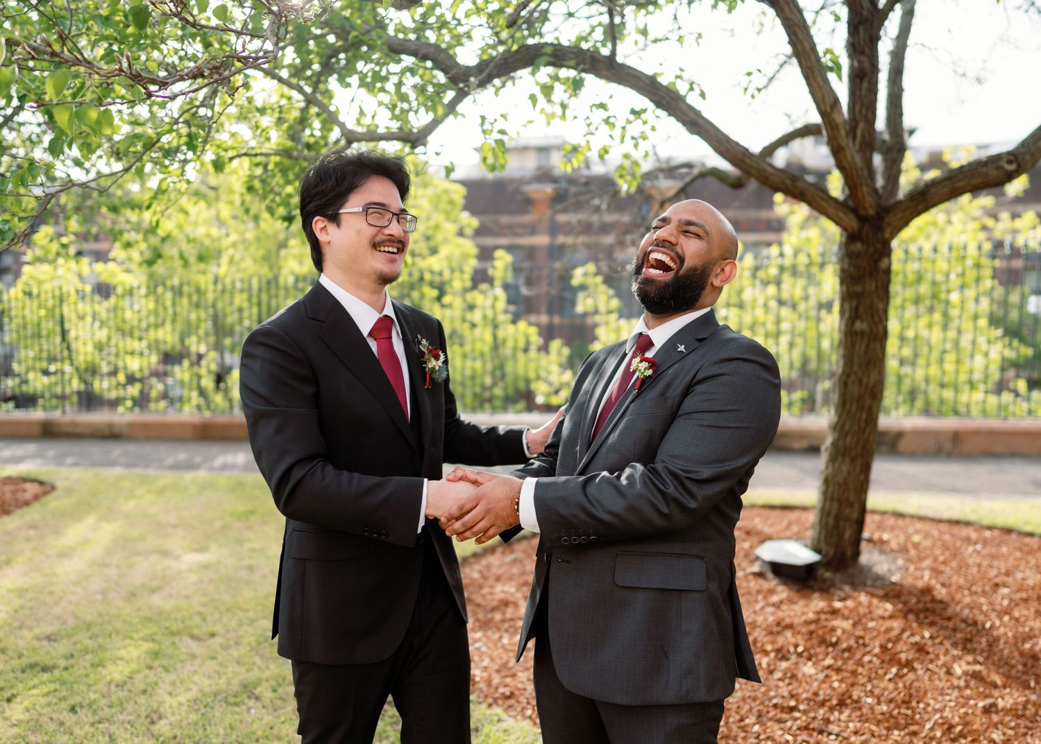 Wedding party members share joyful laughter under trees in an outdoor setting.