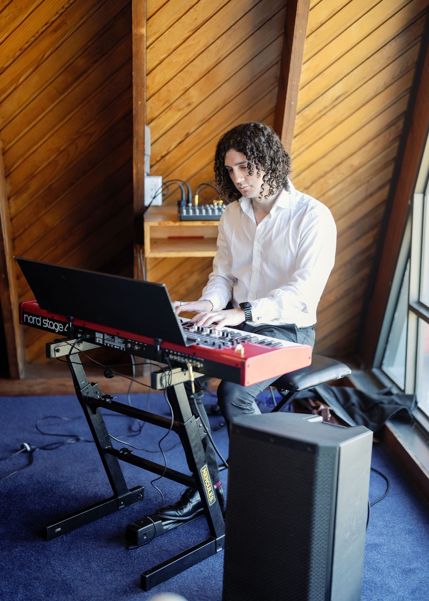 Musical equipment setup in a room with wooden paneled ceiling and blue carpeting.