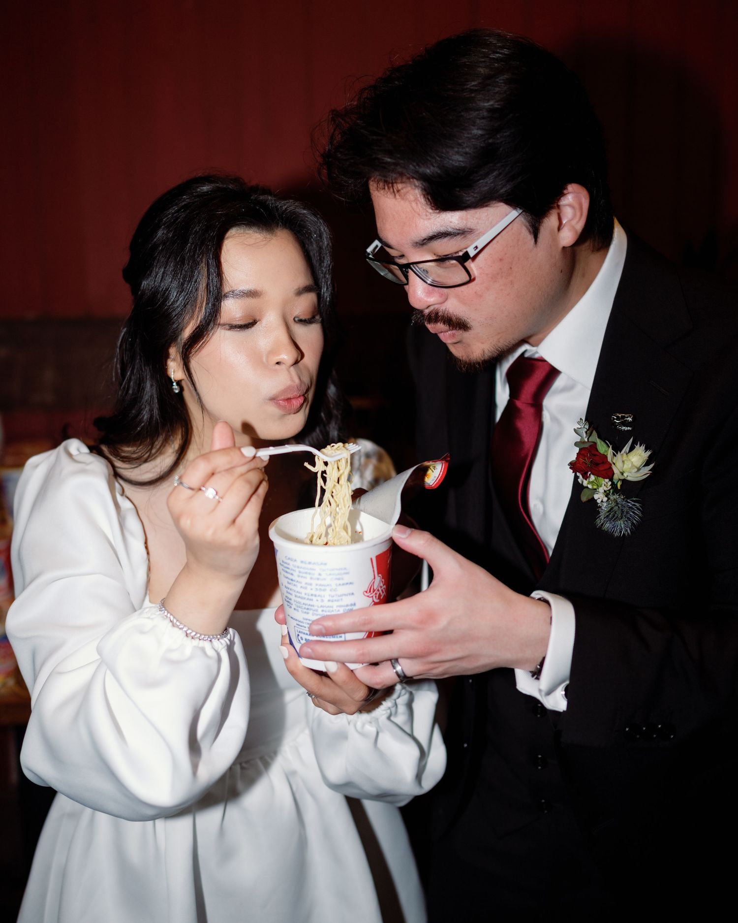 A couple shares a cup of noodles together at their wedding reception.