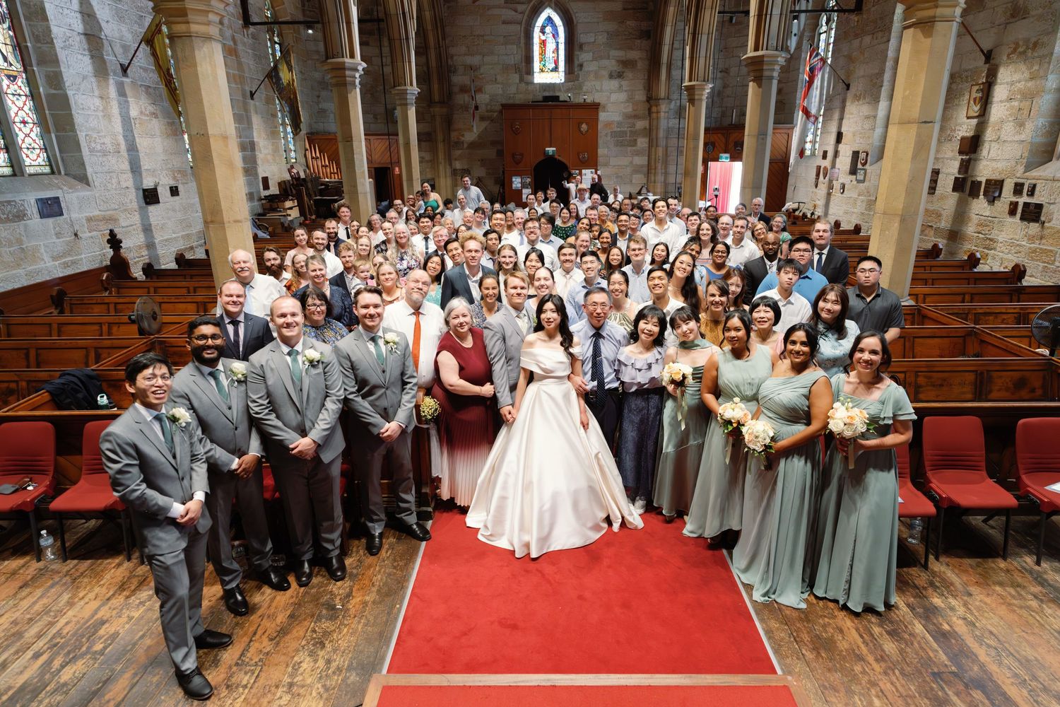 Wide angle view of traditional church wedding ceremony with red carpet aisle and filled pews.