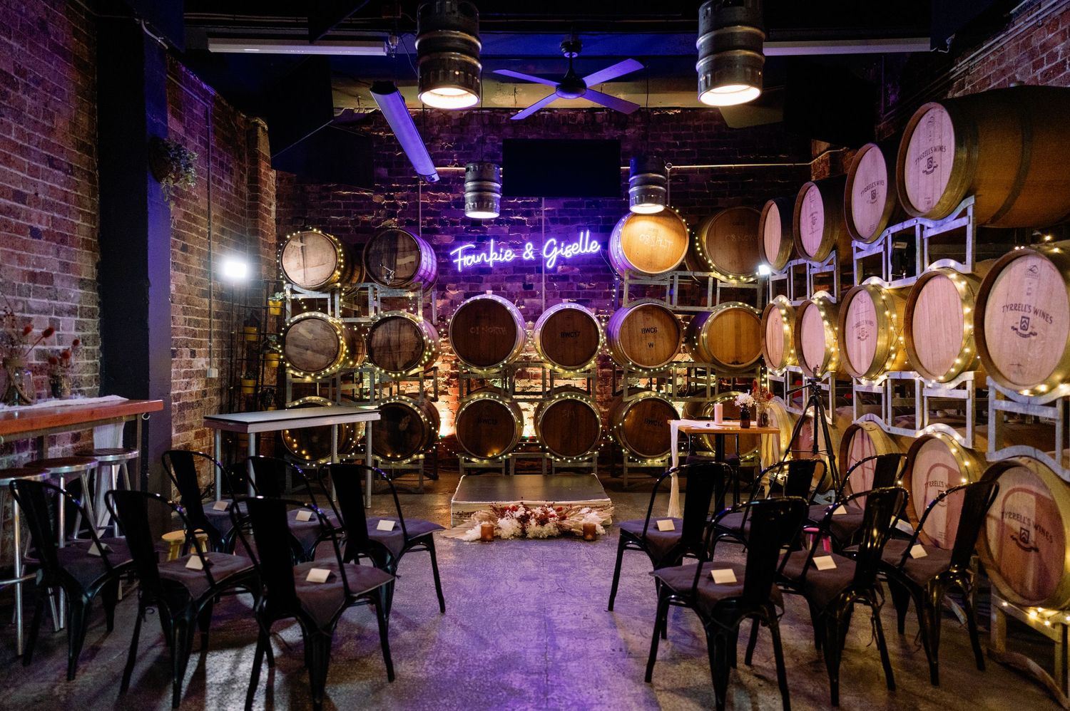 Rustic wine barrel room with wooden barrels stacked along walls and purple ambient lighting creating an intimate atmosphere.