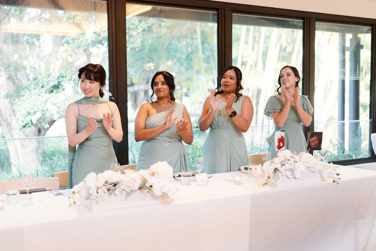 Row of bridesmaids in formal attire seated at a wedding reception table.