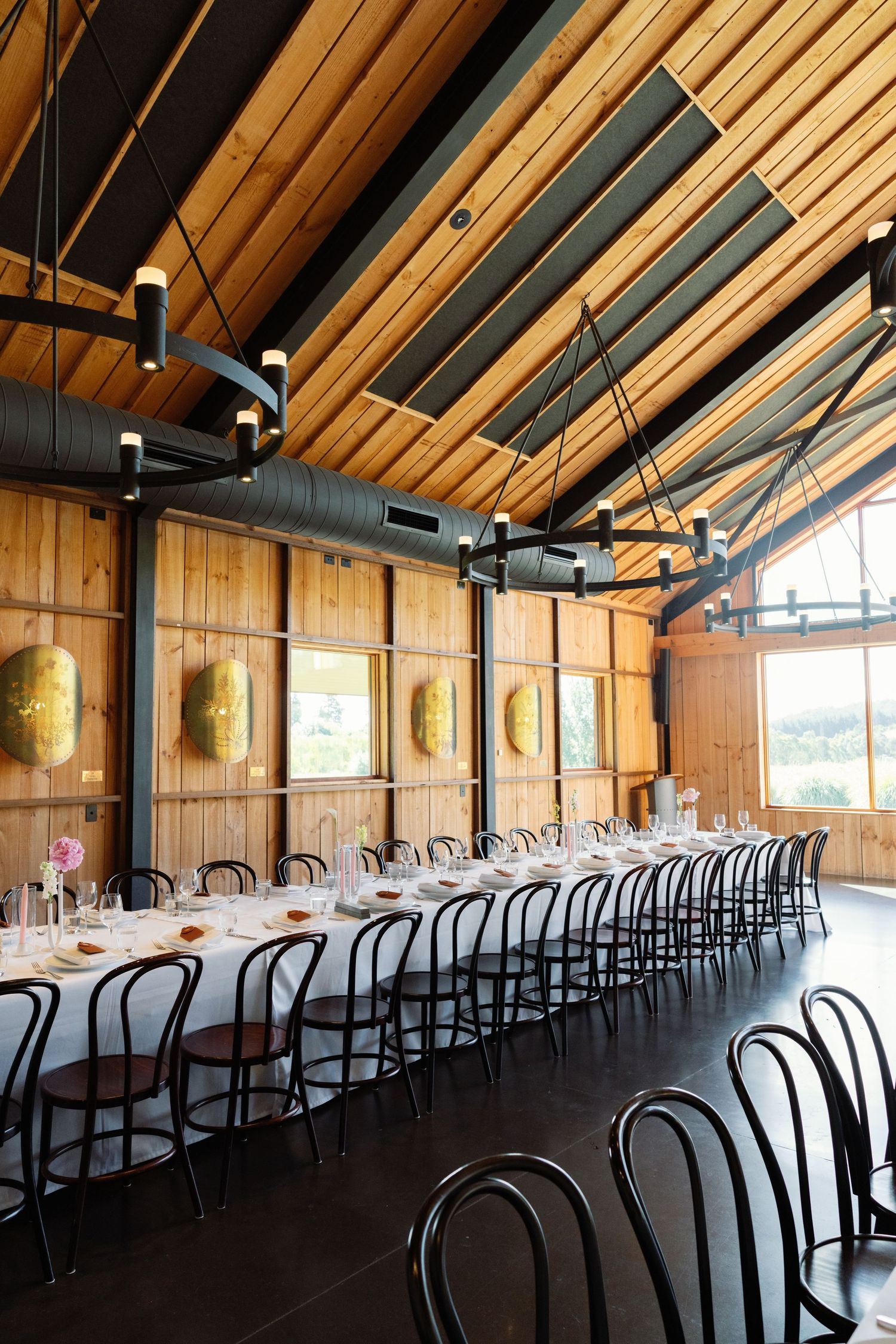 Modern rustic wedding venue interior with wooden ceiling beams and rows of bentwood chairs.