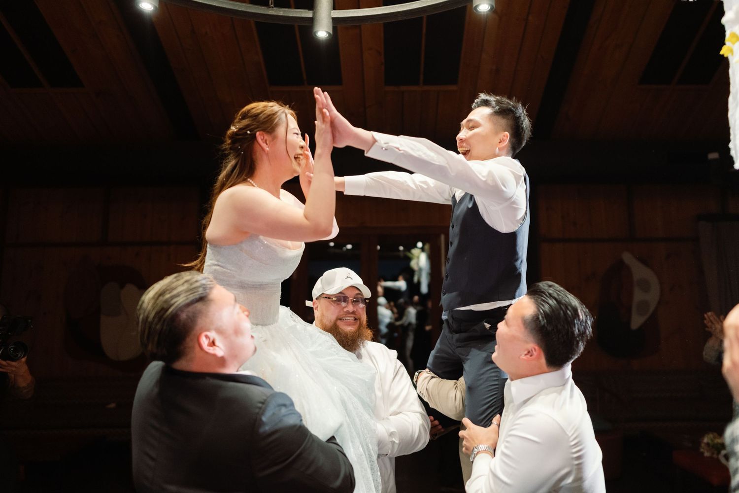 Wedding guests lift and celebrate during a lively dance floor moment.