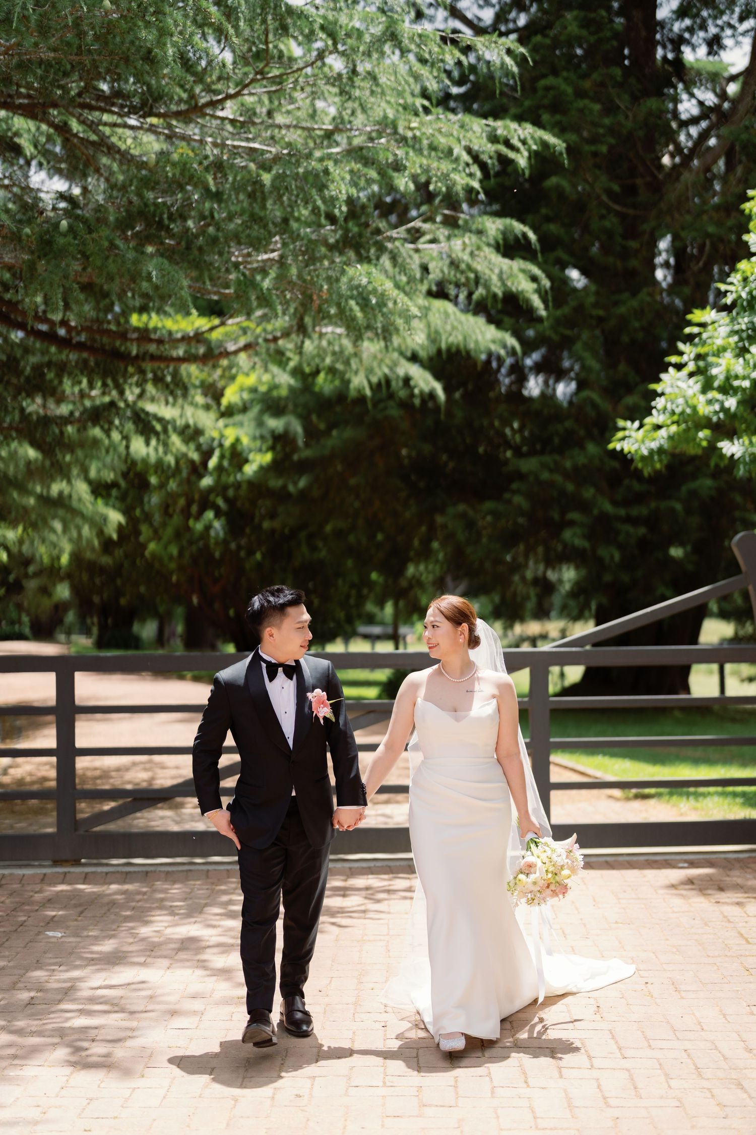 A couple walking along a tree-lined brick pathway in formal attire.