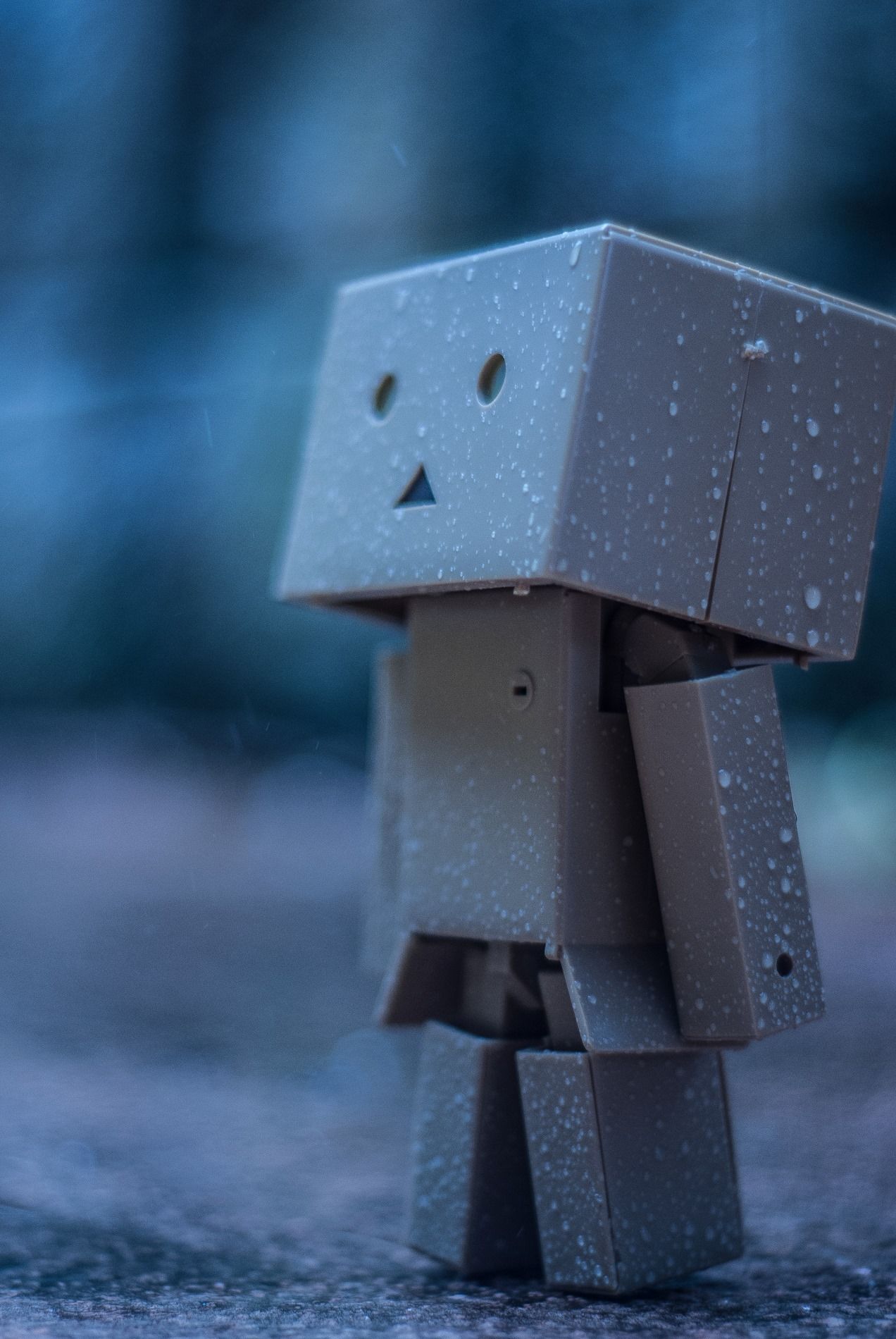 A cardboard robot figure with a simple face standing in the rain.