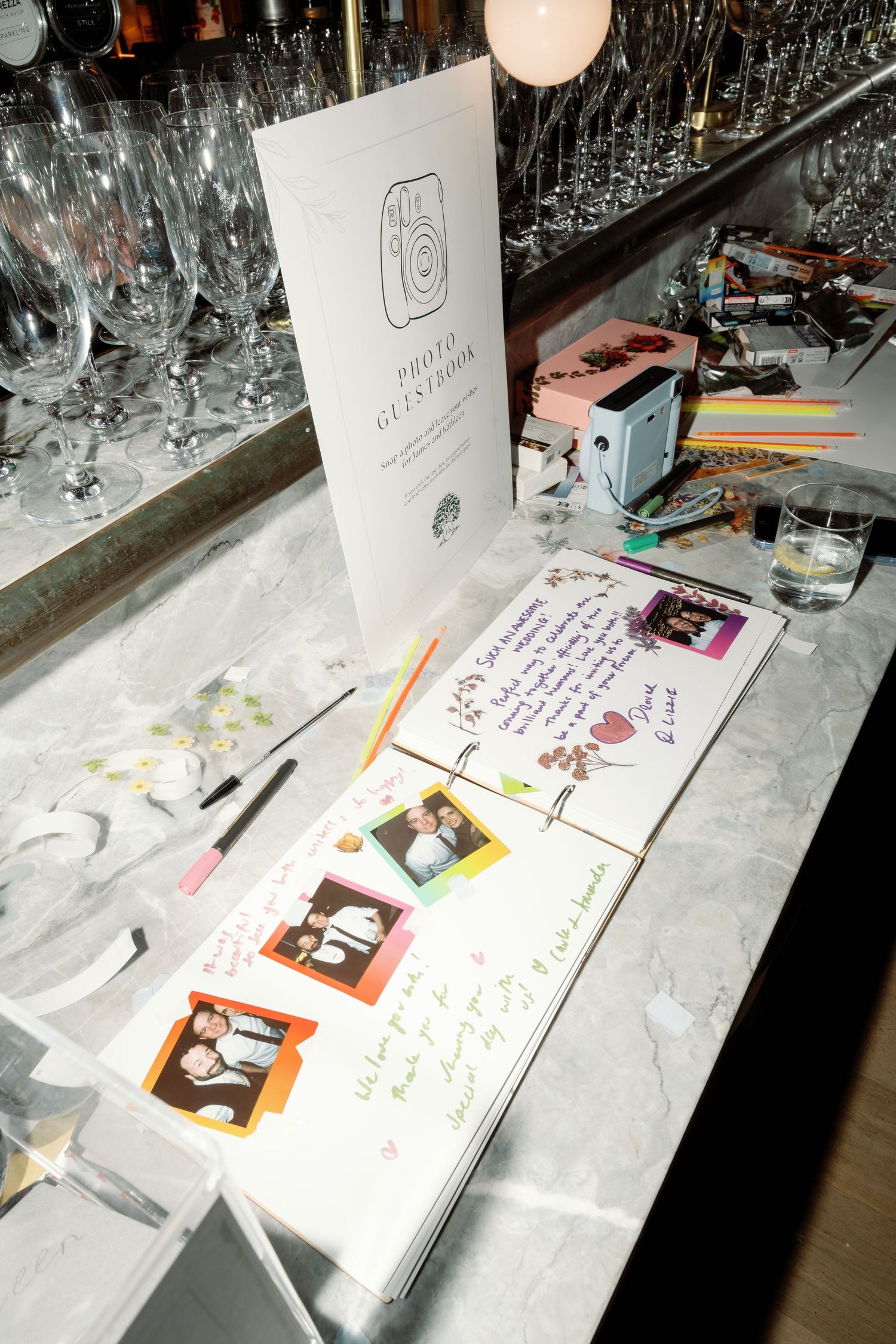 A wedding photo guestbook with Polaroid photos and handwritten messages displayed on a marble bar counter.