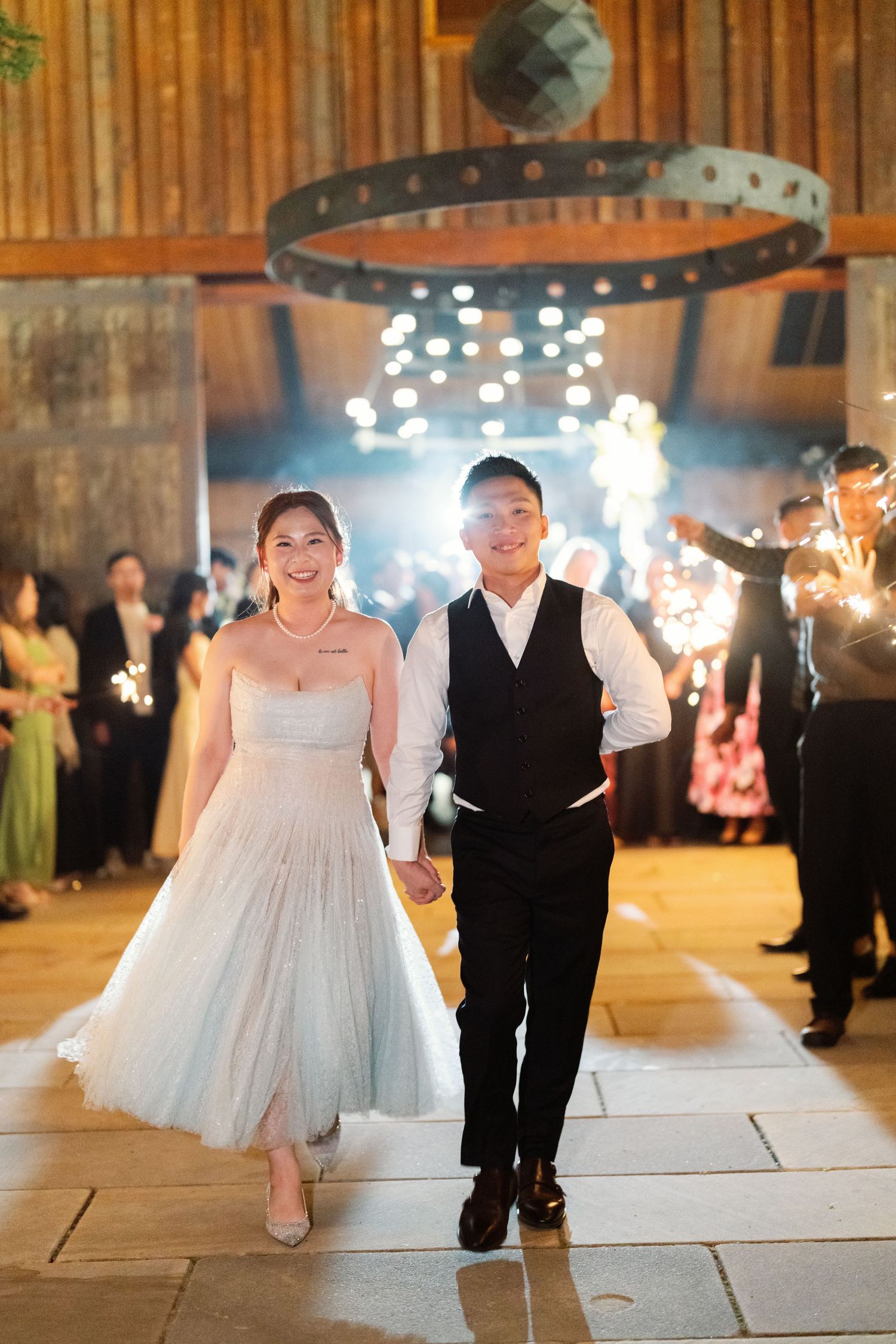 Grand wedding exit with sparklers under industrial chandelier in elegant barn venue.