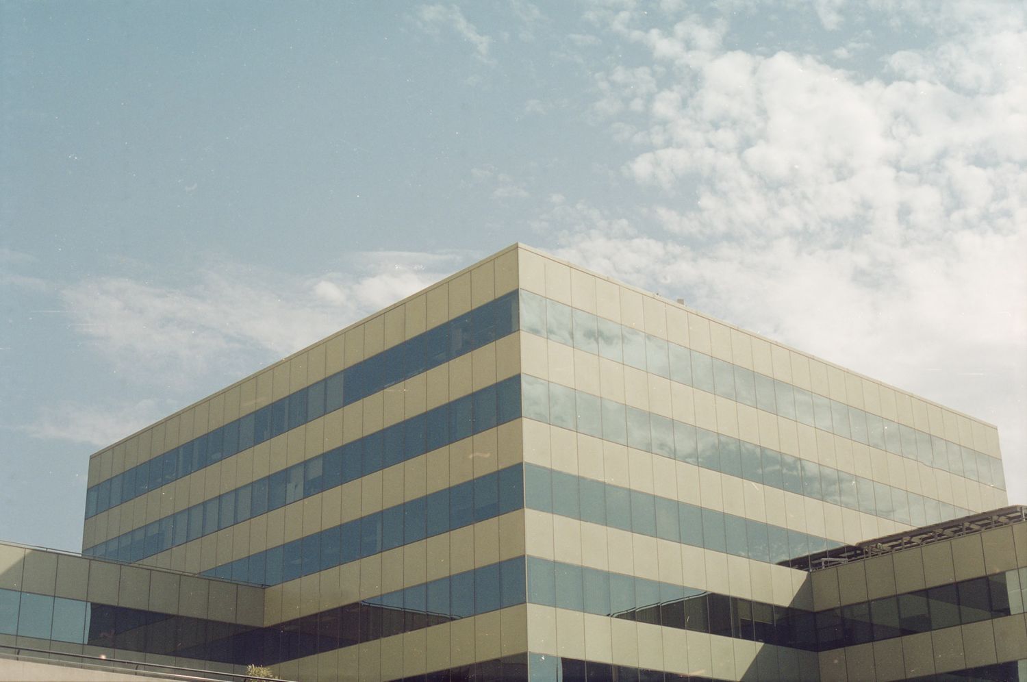 Modern office building with geometric design against blue sky with white clouds.