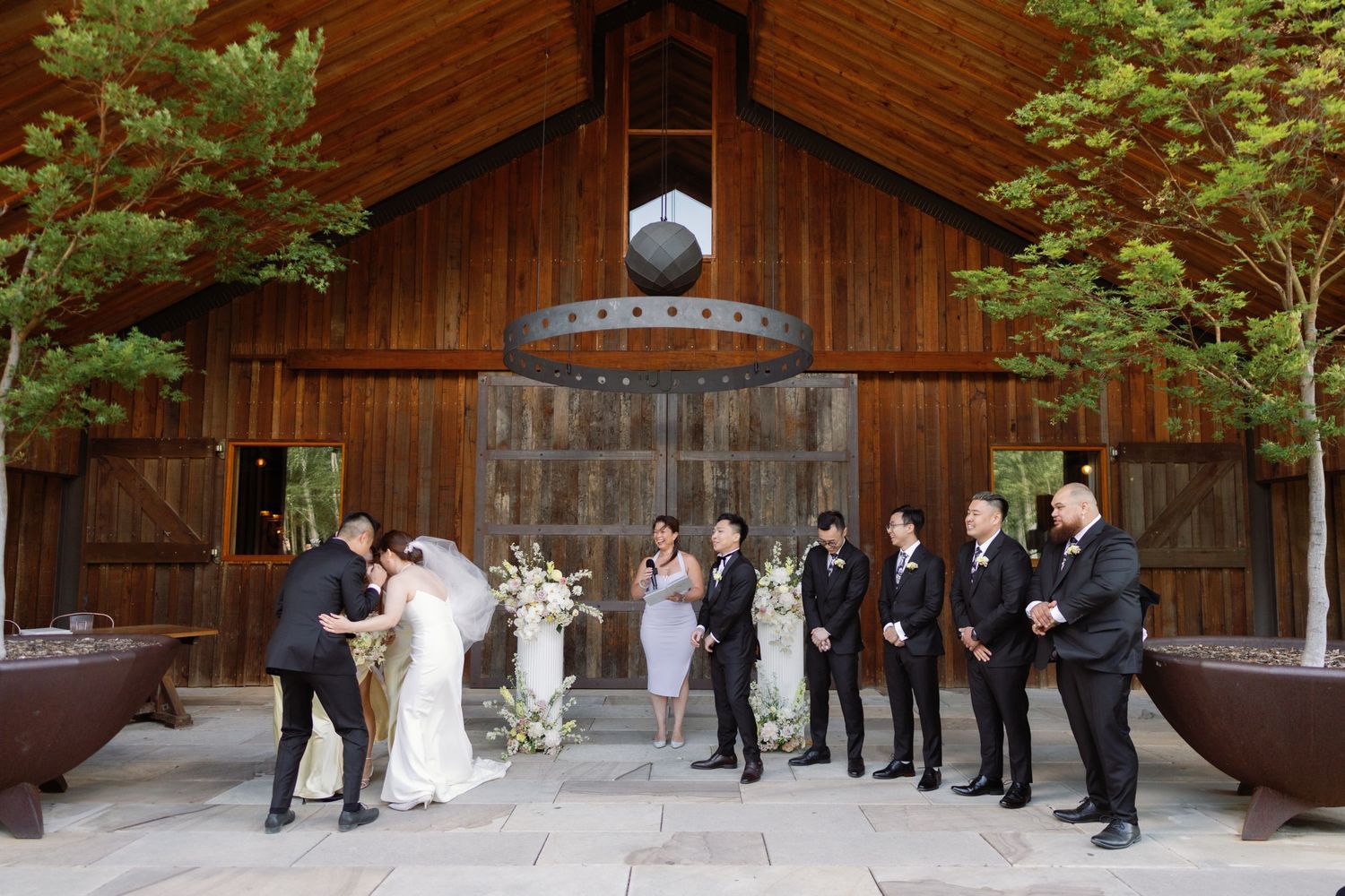Wedding party lines up against rustic wooden barn wall for formal group photos.