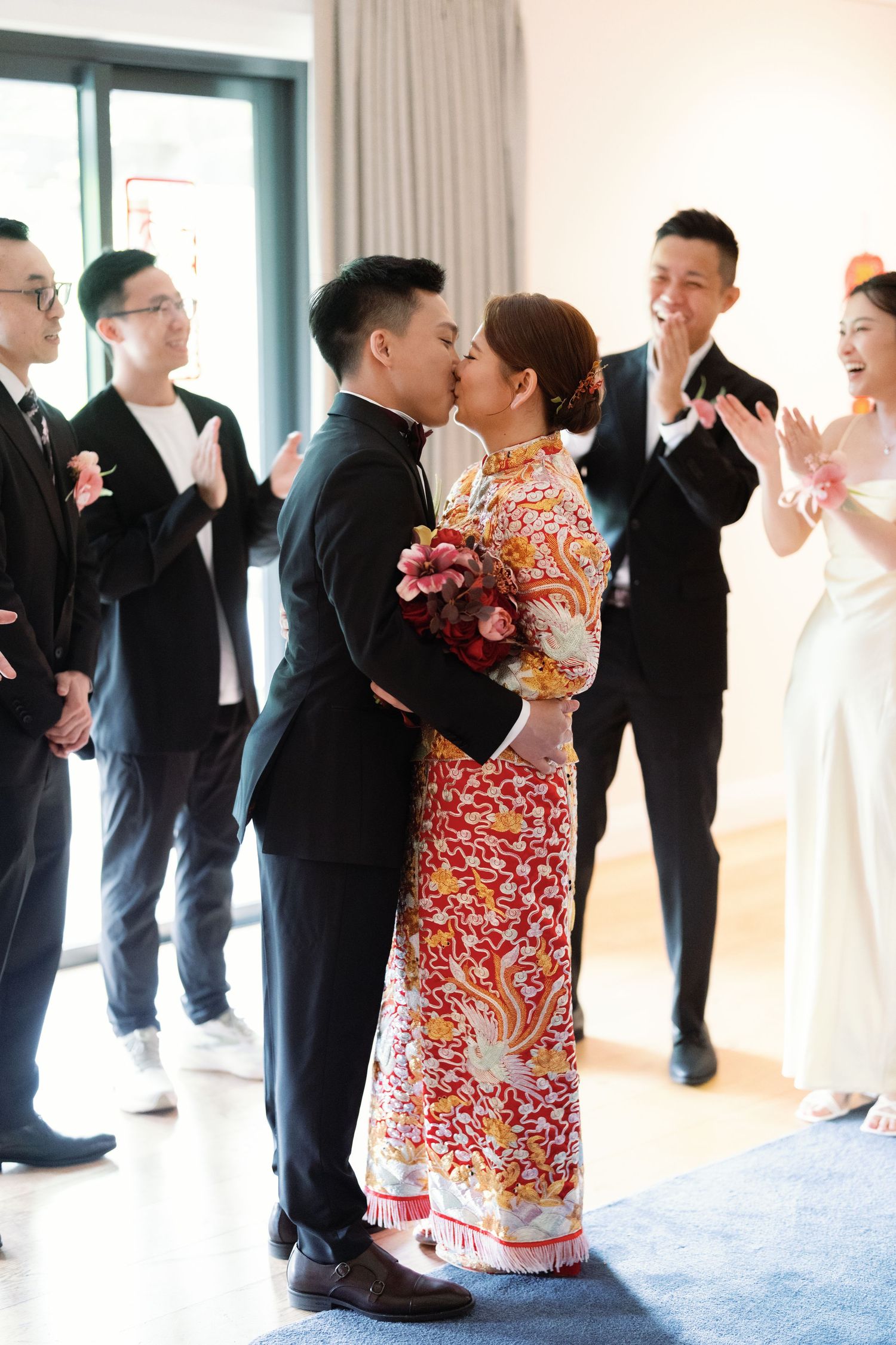A couple shares a kiss while wedding guests applaud in a bright indoor setting.