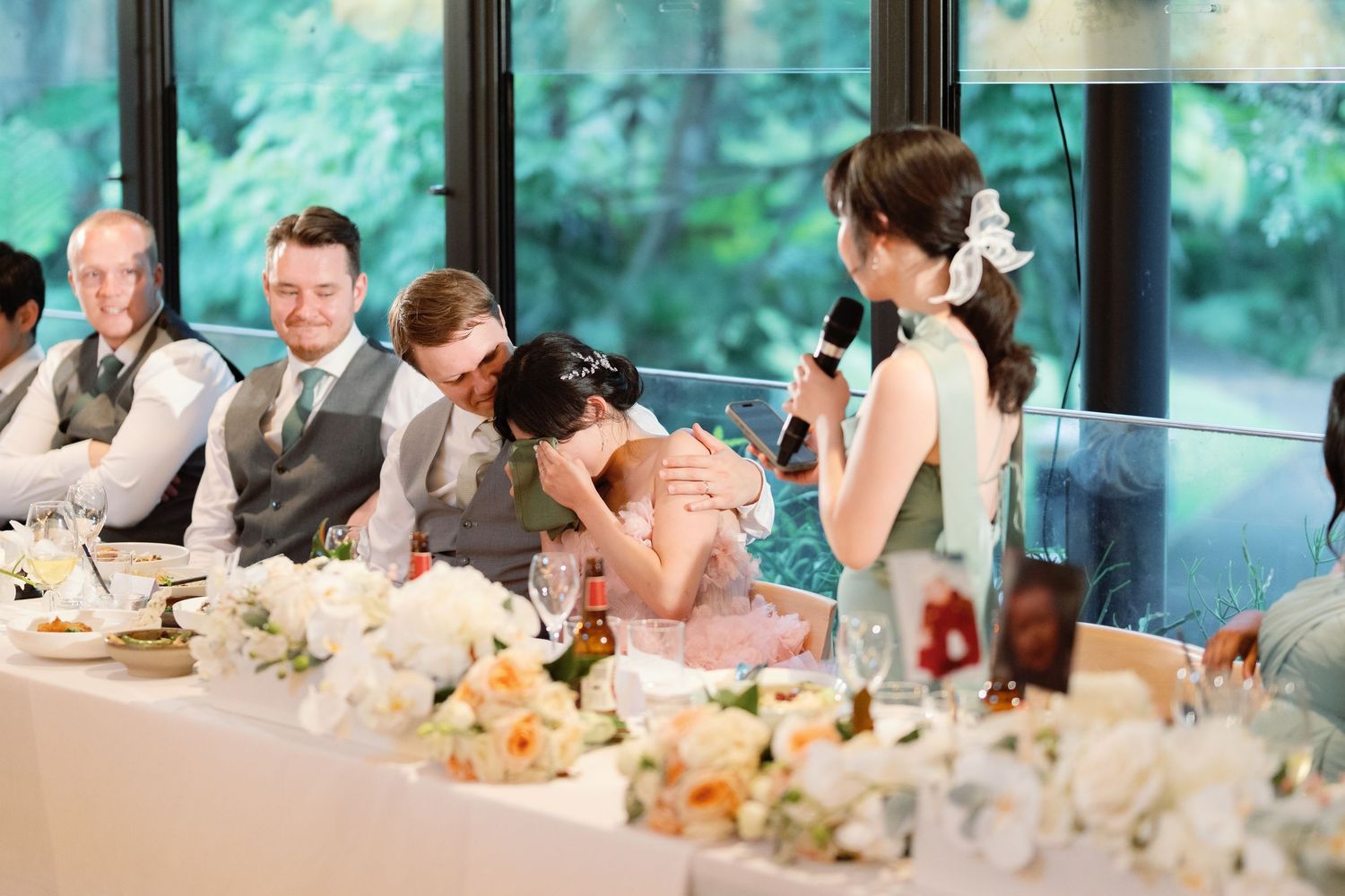 Wedding guests seated at reception tables with decorative centerpieces and aqua-colored backdrop.