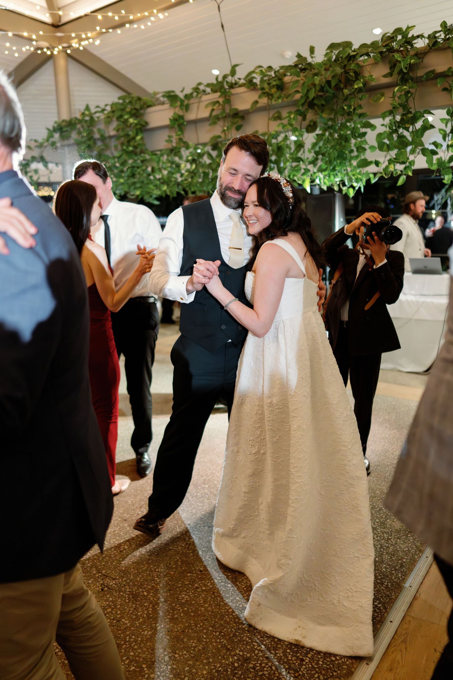 Bride and groom share first dance under string lights and greenery at elegant wedding reception.