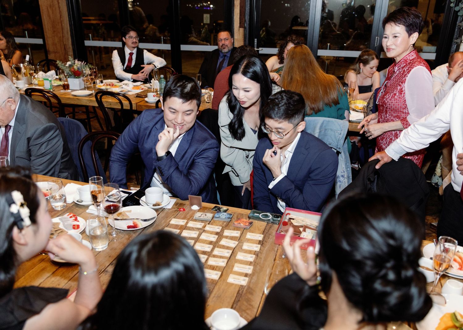 Wedding reception guests enjoying conversation and food at long wooden tables.