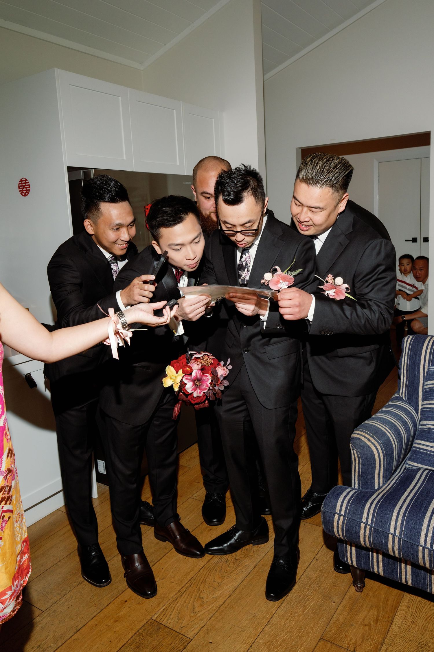 Group wearing formal black suits lined up on blue striped couch during wedding festivities.