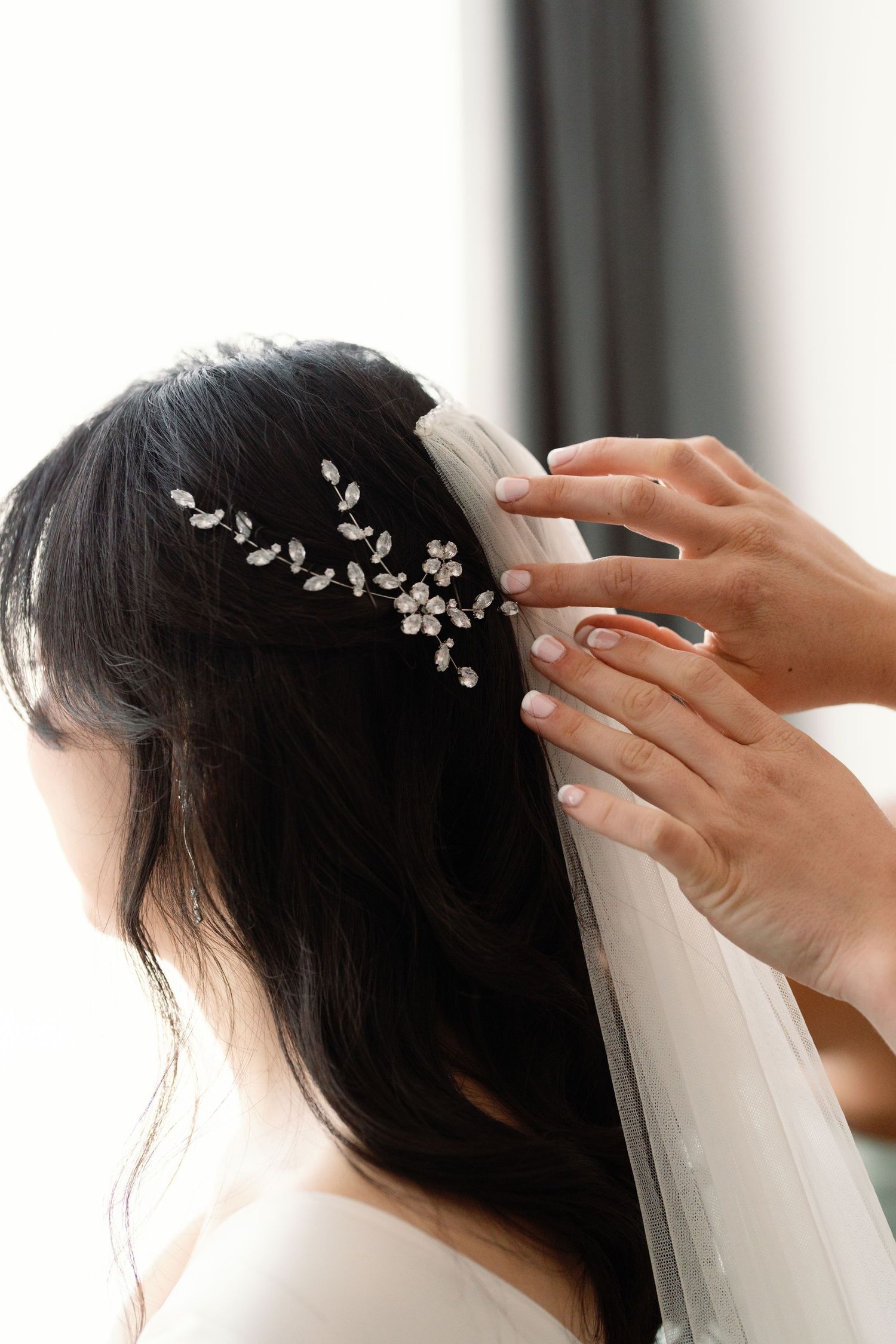 Delicate floral hair accessories being placed in dark hair with a white veil.