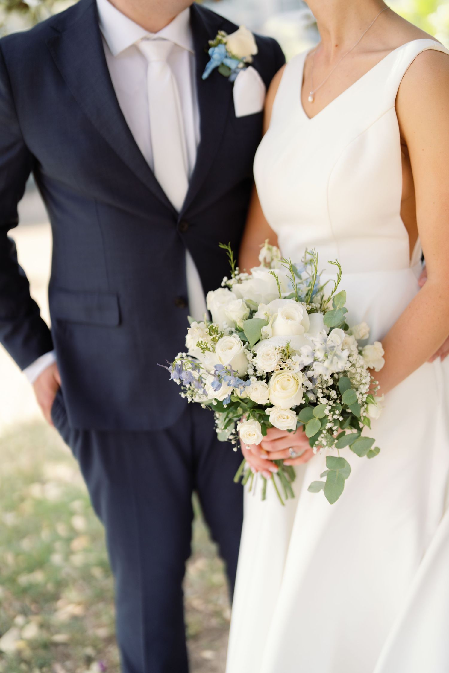 Elegant wedding party members hold white floral bouquets while wearing navy suits and white dresses.