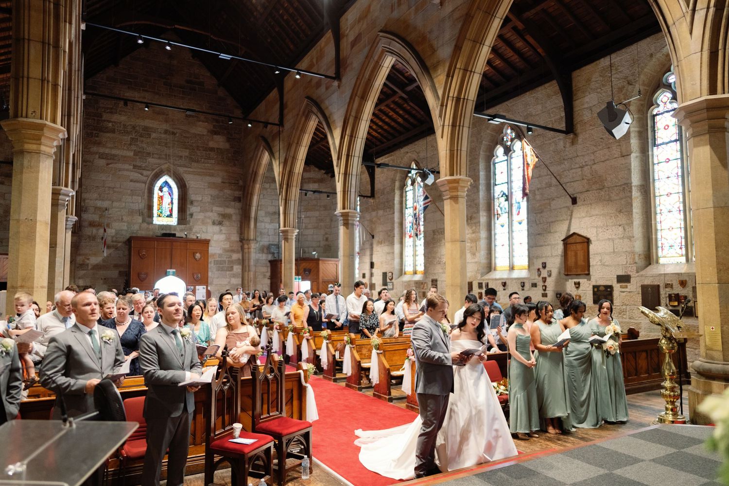 Panoramic view of a church wedding ceremony with guests seated in wooden pews under vaulted ceilings.