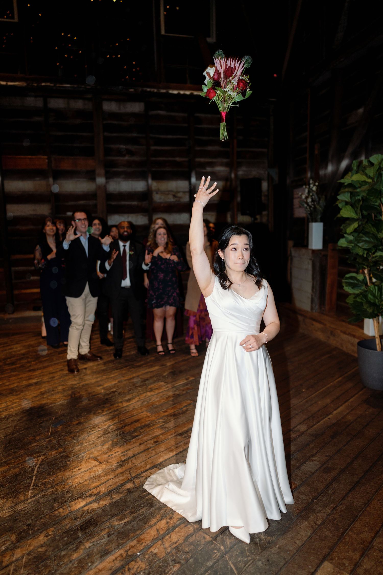A person in a white wedding dress dances on a rustic wooden floor during a celebration.