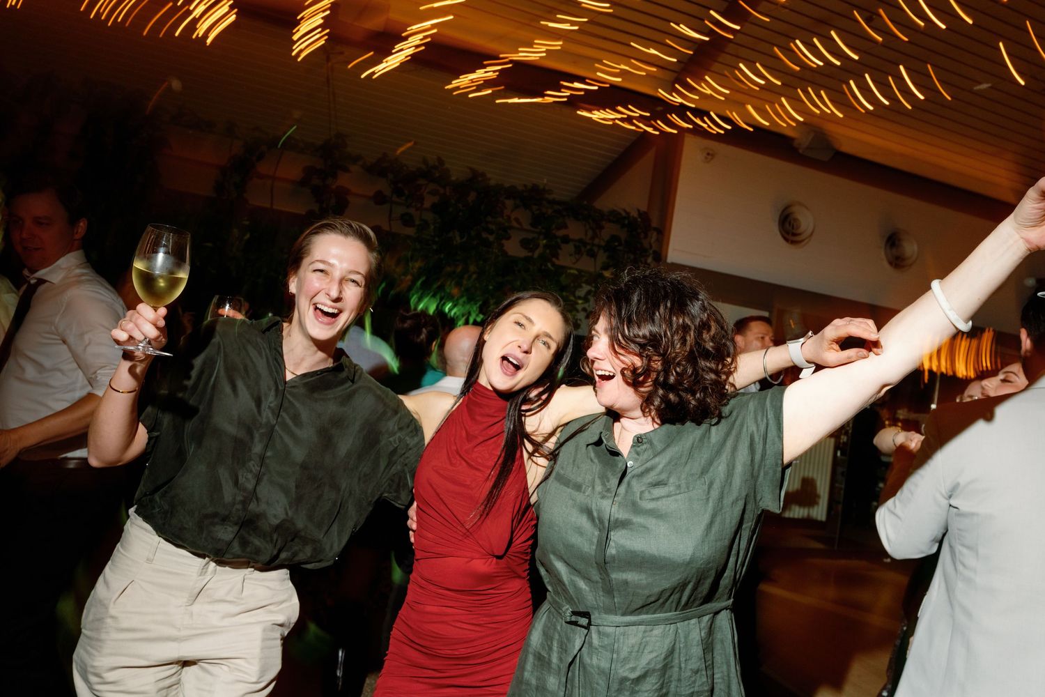 Three joyful women dance and celebrate together on the wedding reception dance floor.
