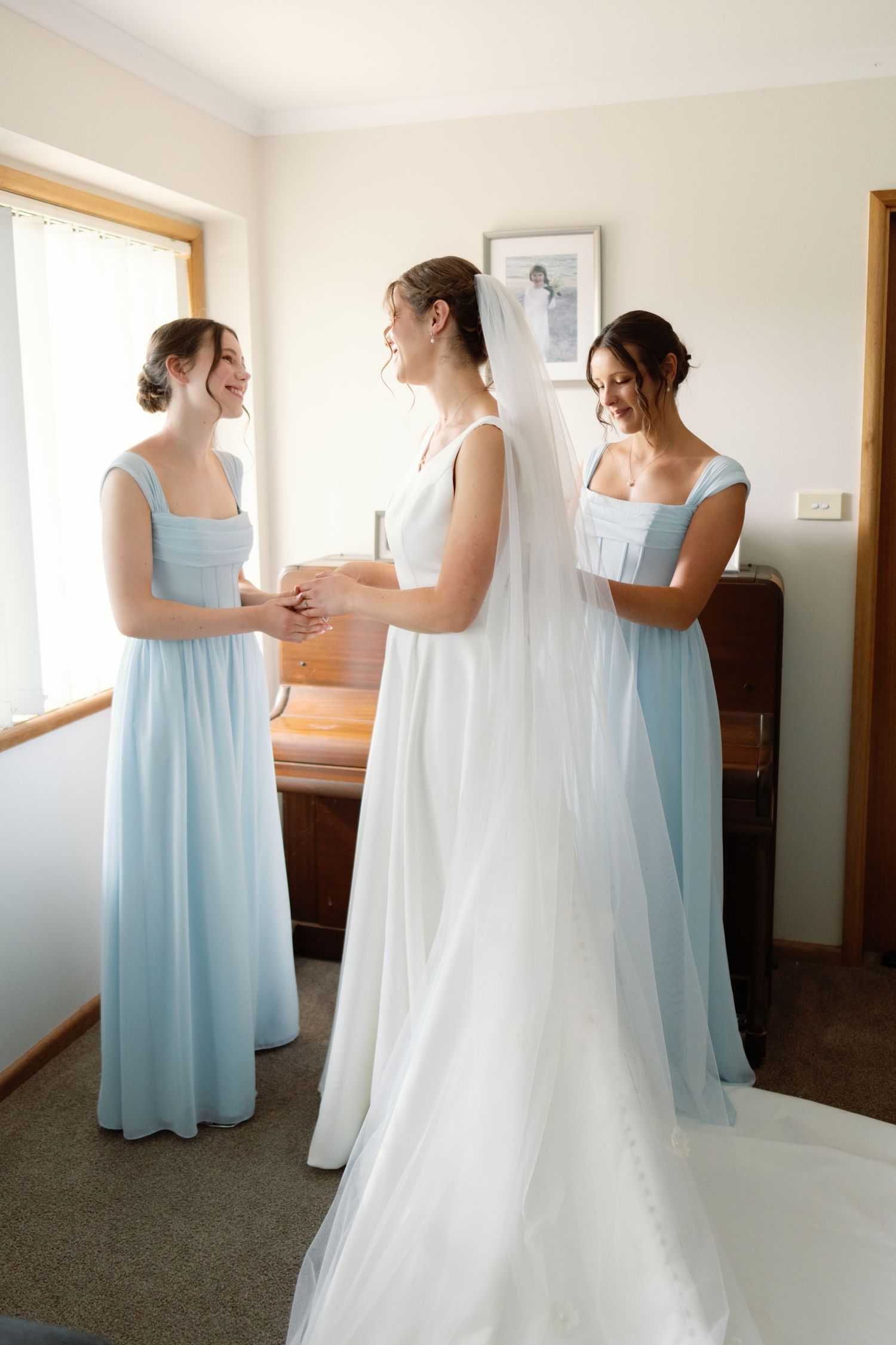Wedding preparations showing bridesmaids in light blue dresses helping with a white wedding gown.