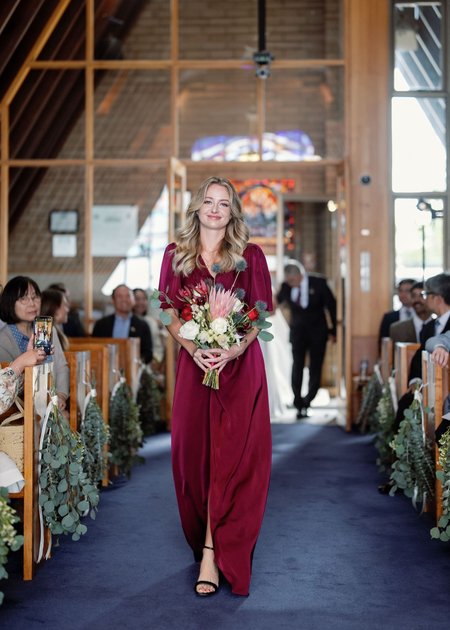 Church aisle decorated with evergreen garlands and wooden pews for a winter wedding ceremony.