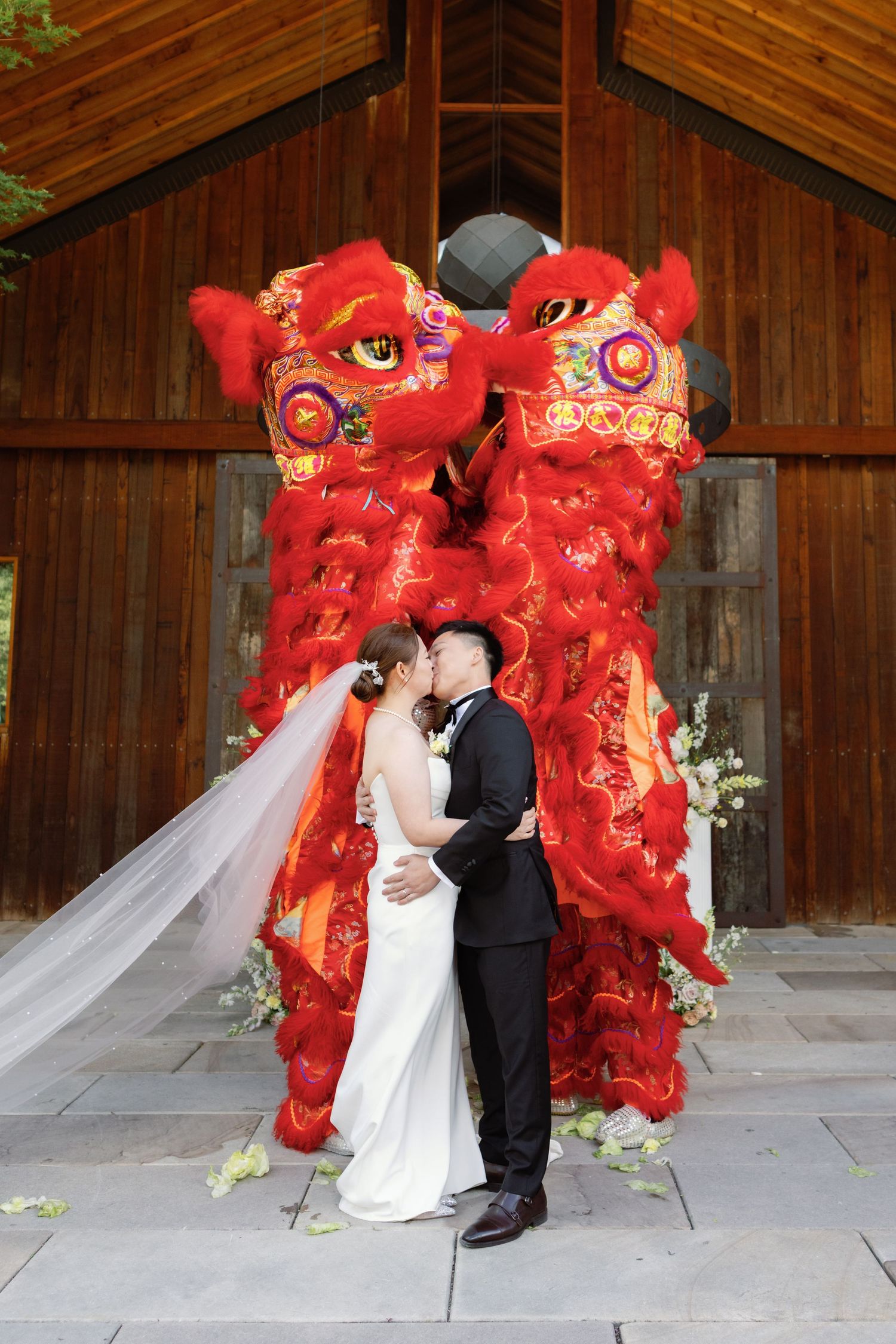 Traditional Chinese red lion dance performers frame a wedding ceremony under a wooden pavilion.