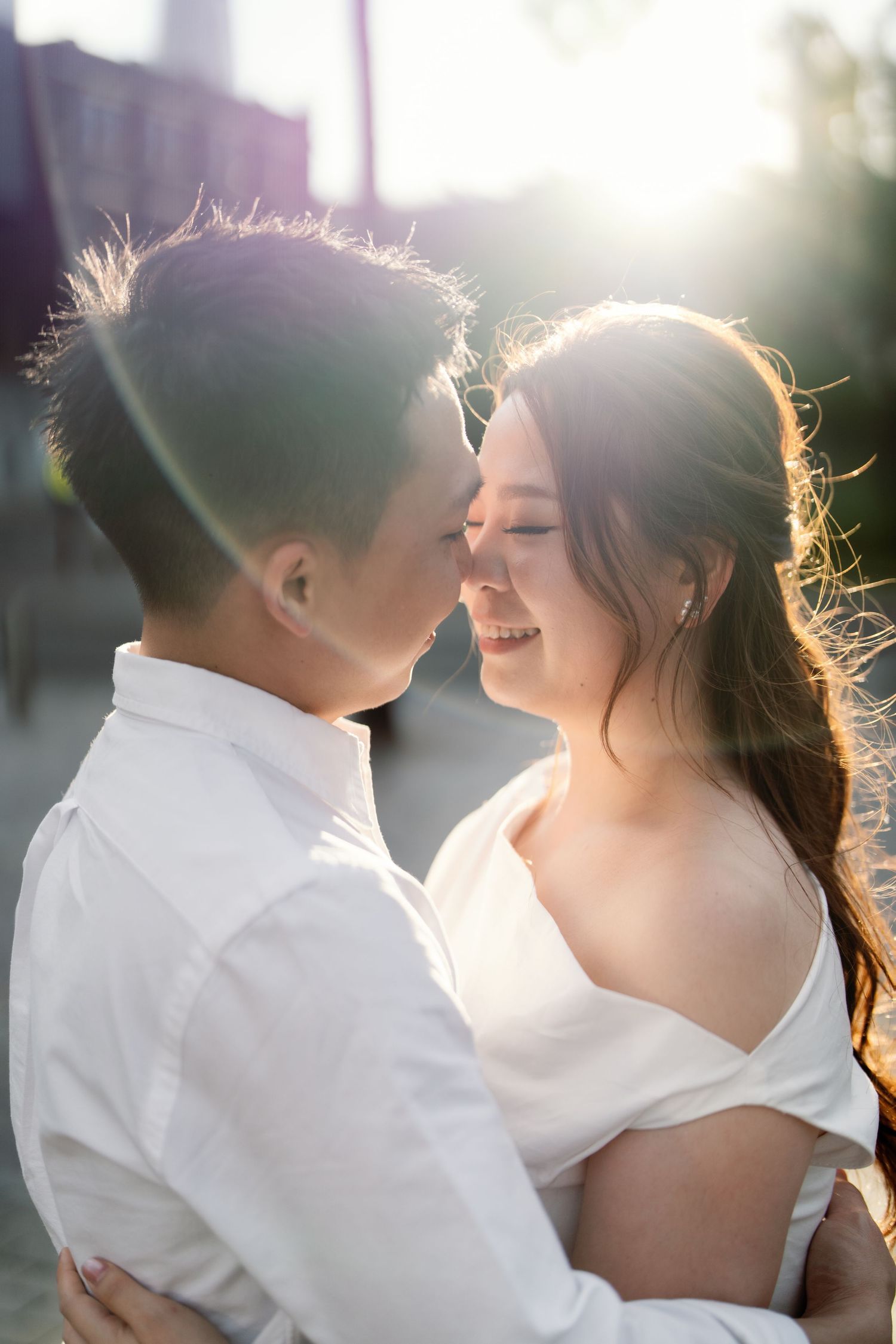 A romantic couple embraces in soft sunlight during their engagement photo session, creating a dreamy backlit effect.