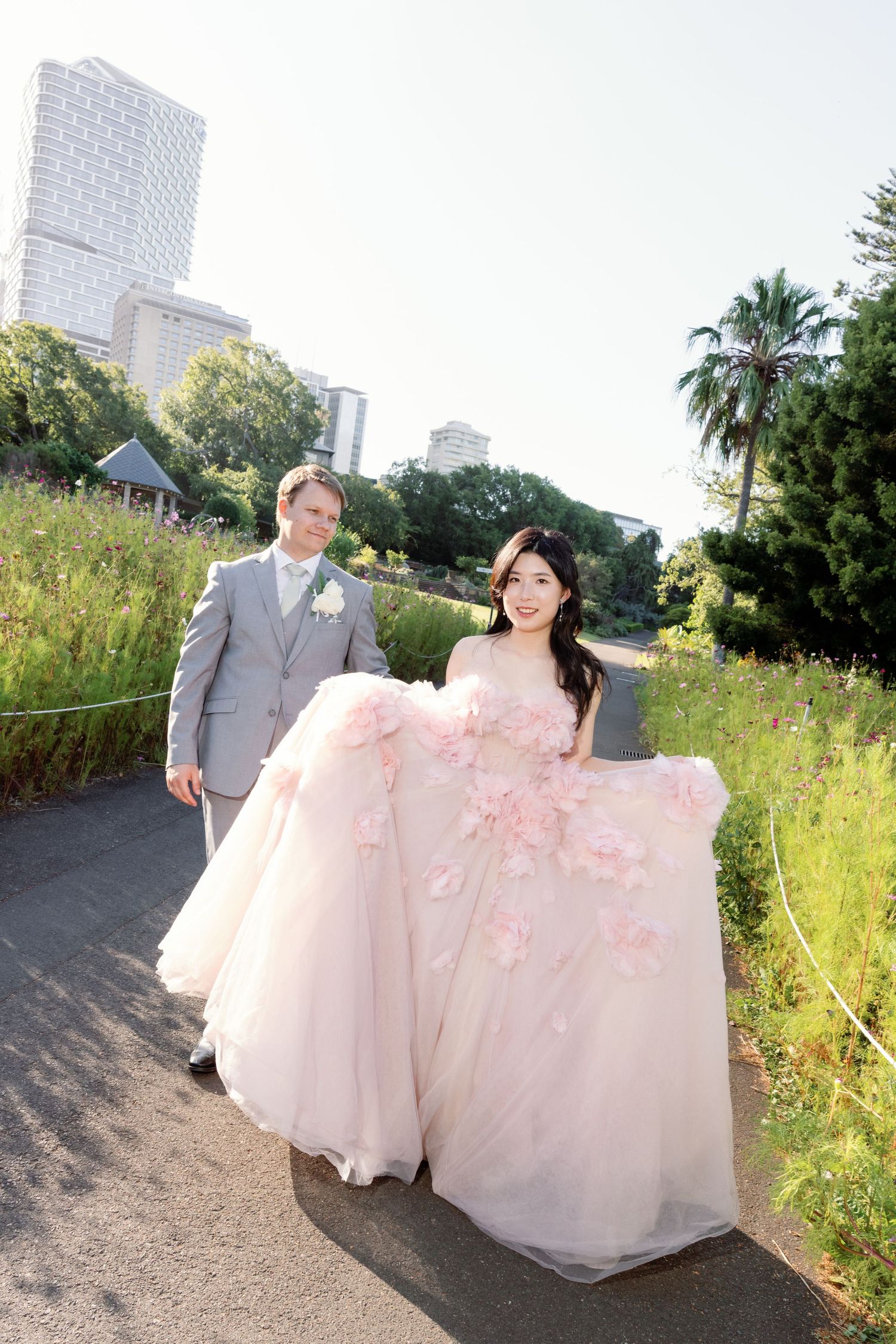 Couple walks along urban path with city skyline and palm trees visible in background.