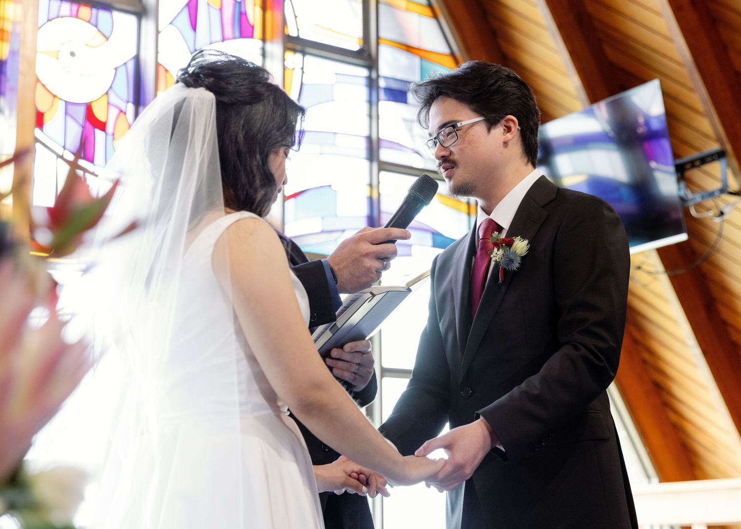 Wedding ceremony taking place in a church with wooden beams and stained glass windows.