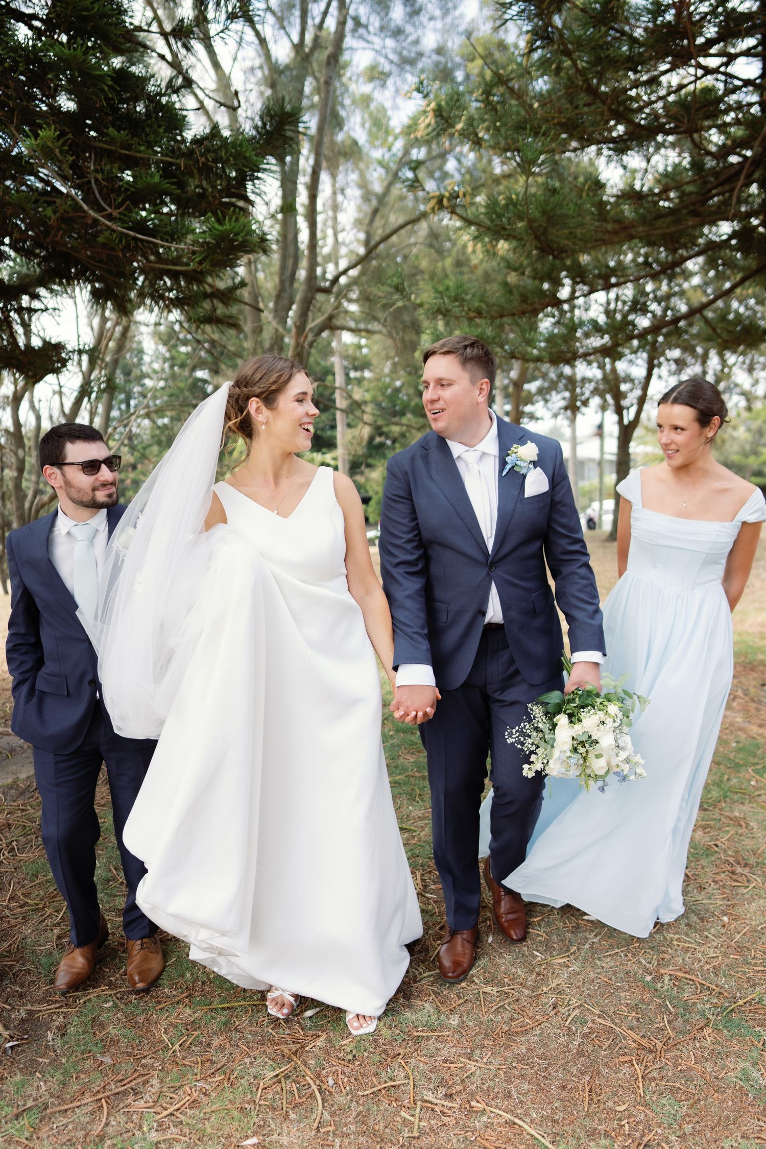 Wedding party walking and laughing together through a wooded outdoor setting.
