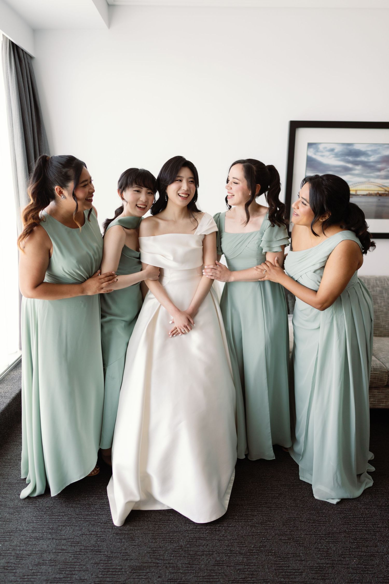 Bridesmaids in mint green dresses pose together with the bride in white.