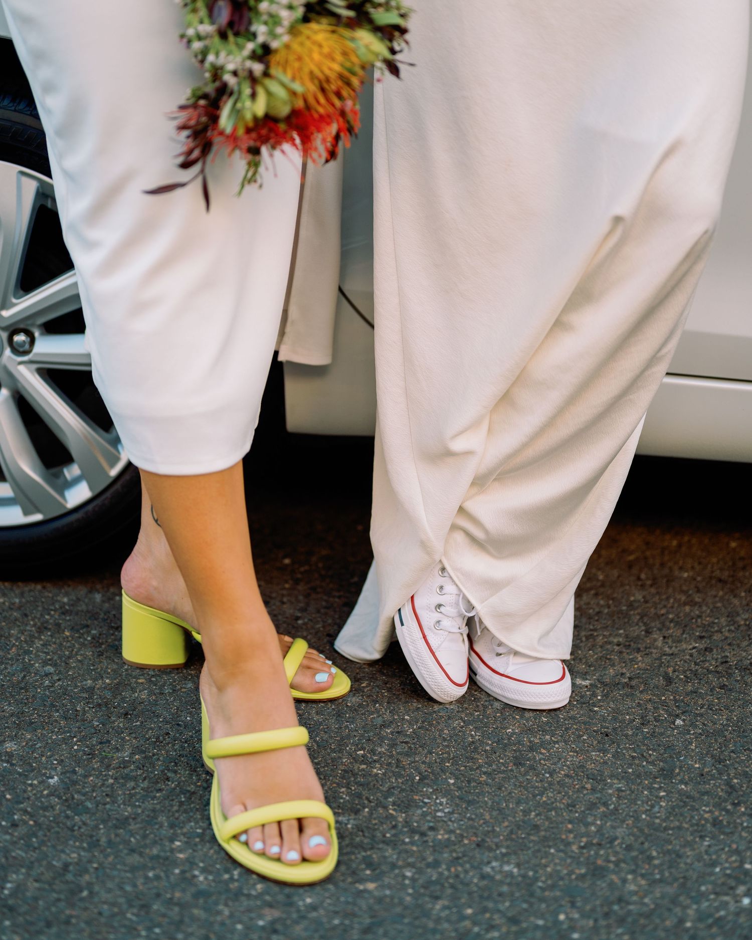 Close-up of bridesmaids' feet wearing white dresses and colorful sandals at a wedding.
